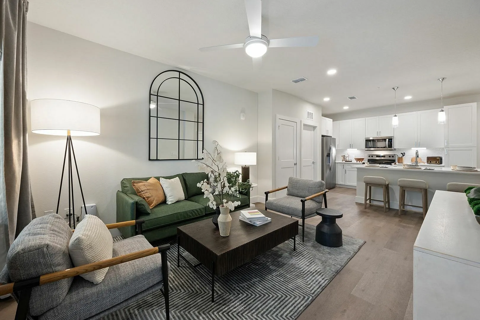 Modern open-plan living room with a green sofa, stylish armchairs, and a spacious kitchen in view.