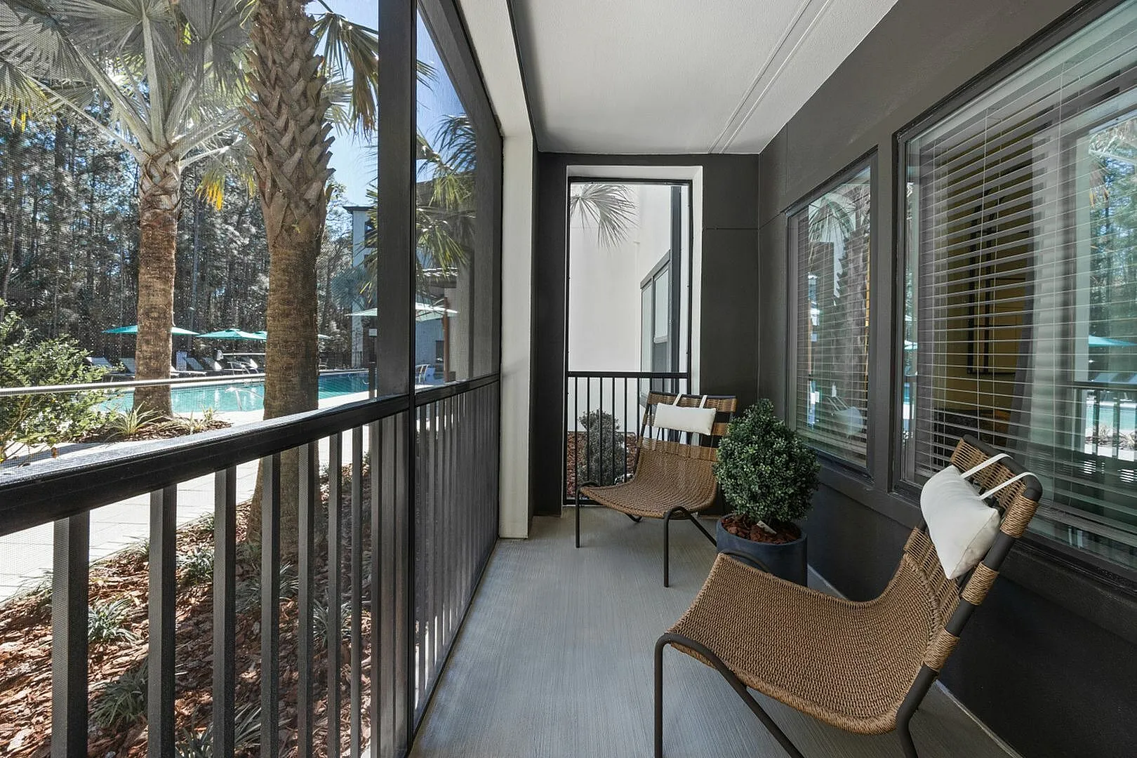 Sunny balcony with wicker chairs overlooking a lush pool area.