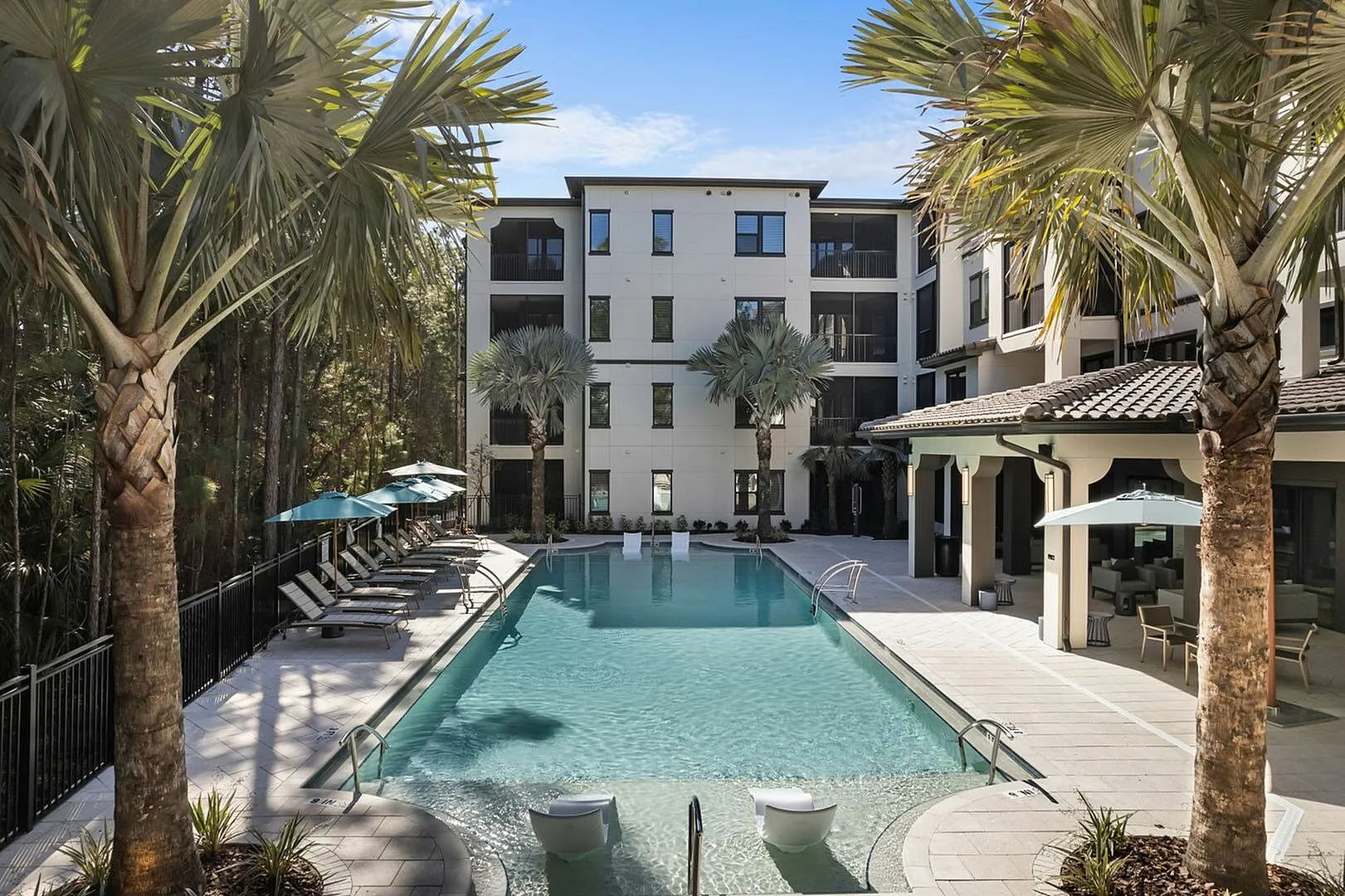 Modern apartment complex with a luxurious swimming pool surrounded by palm trees and sun loungers.
