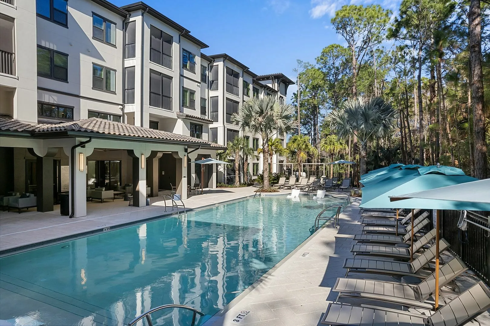 Modern apartment complex with a pristine swimming pool surrounded by lush greenery and sun loungers.