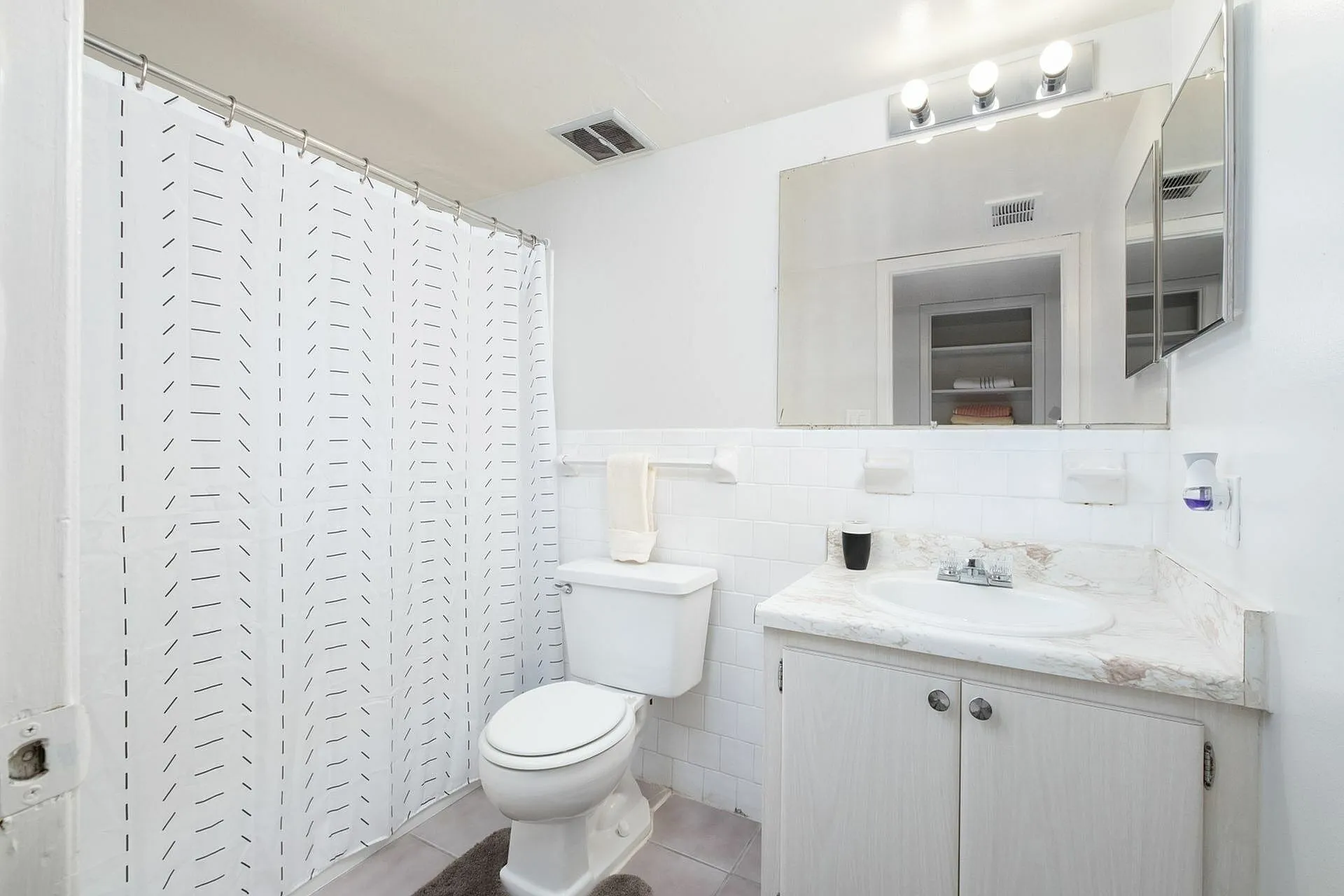 Bright bathroom featuring a modern white vanity, textured shower curtain, and large mirror.