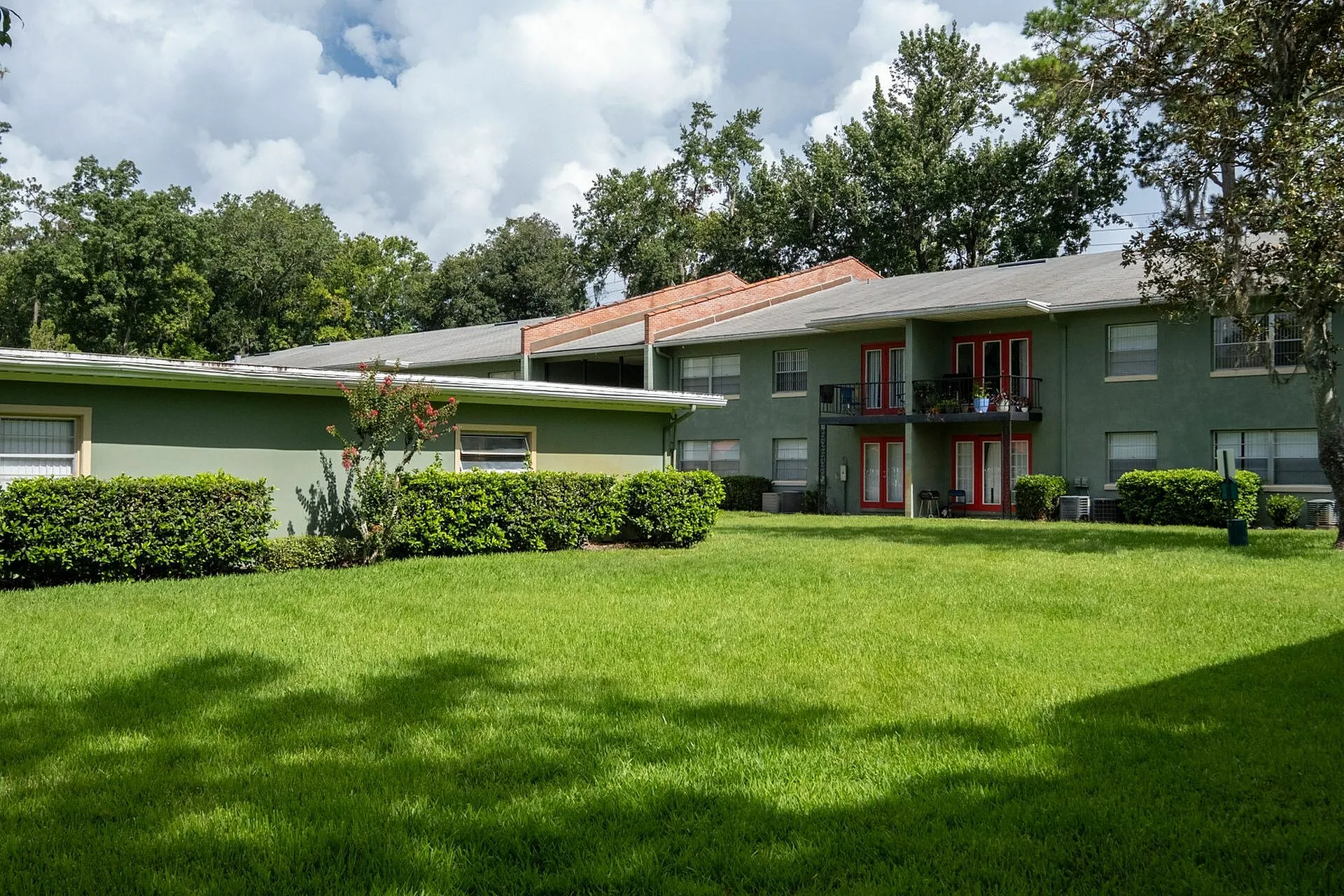 Beautiful apartment complex with lush green lawn, red accents, and a serene outdoor environment.