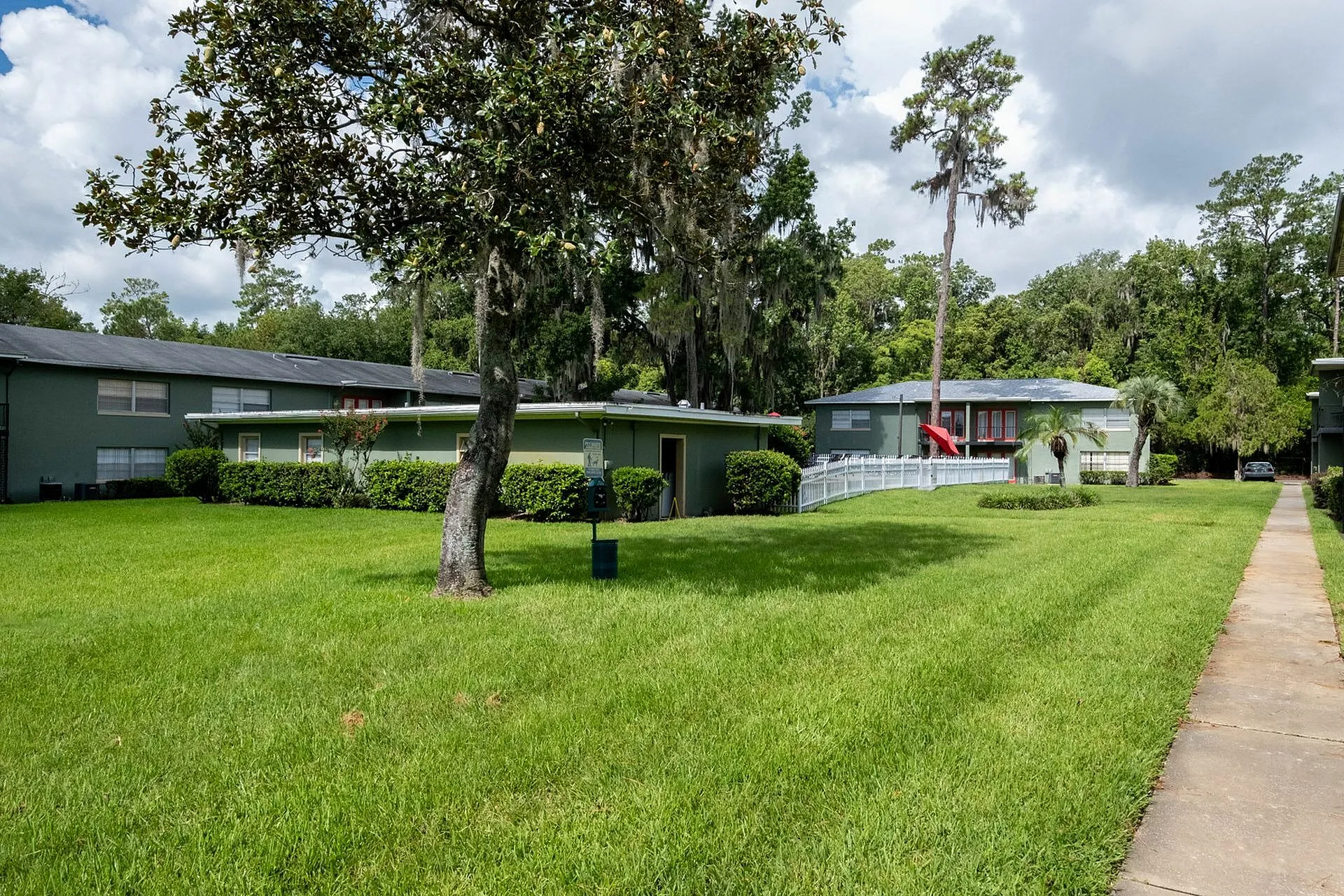 Charming apartment complex with lush green lawns and mature trees under a bright blue sky.