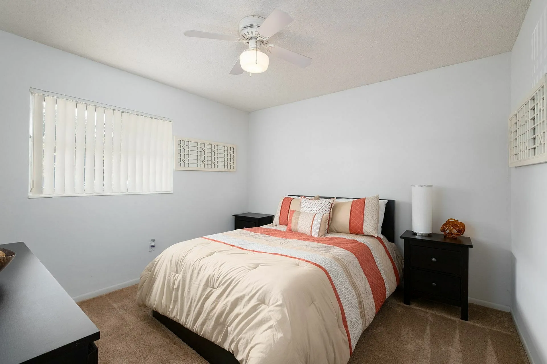 Bright bedroom featuring a comfortable bed with decorative pillows, stylish side tables, and soft carpet flooring.