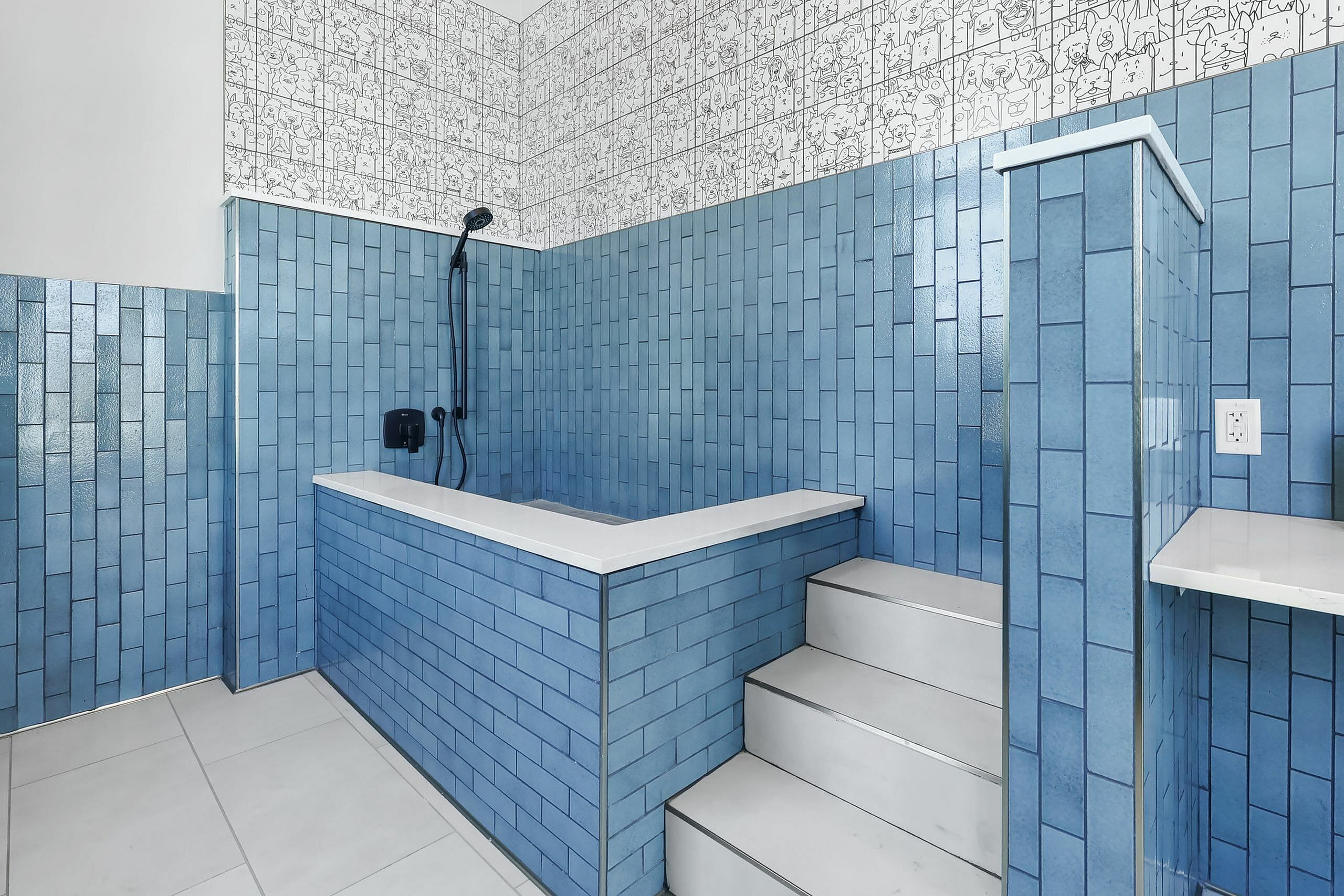 Chic bathroom with vibrant blue tiles, unique cartoon-themed wall design, and elegant built-in steps leading to a luxurious tub.