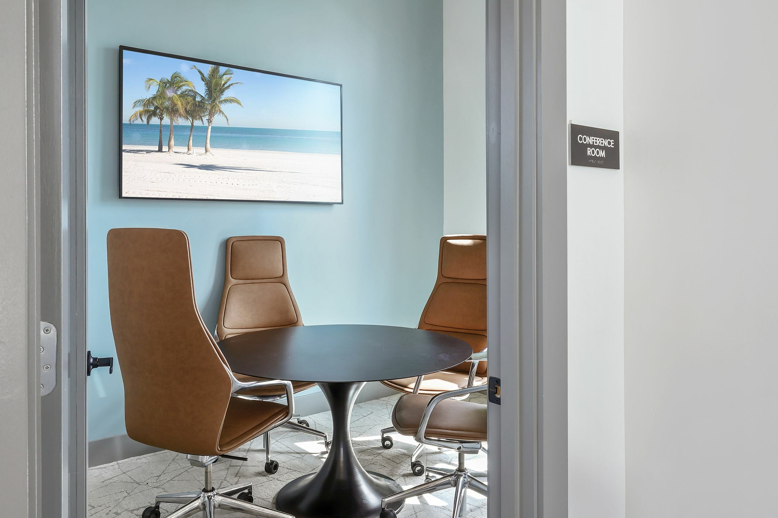 Inviting conference room with a round table, stylish leather chairs, and tropical beach artwork creating a serene ambiance.