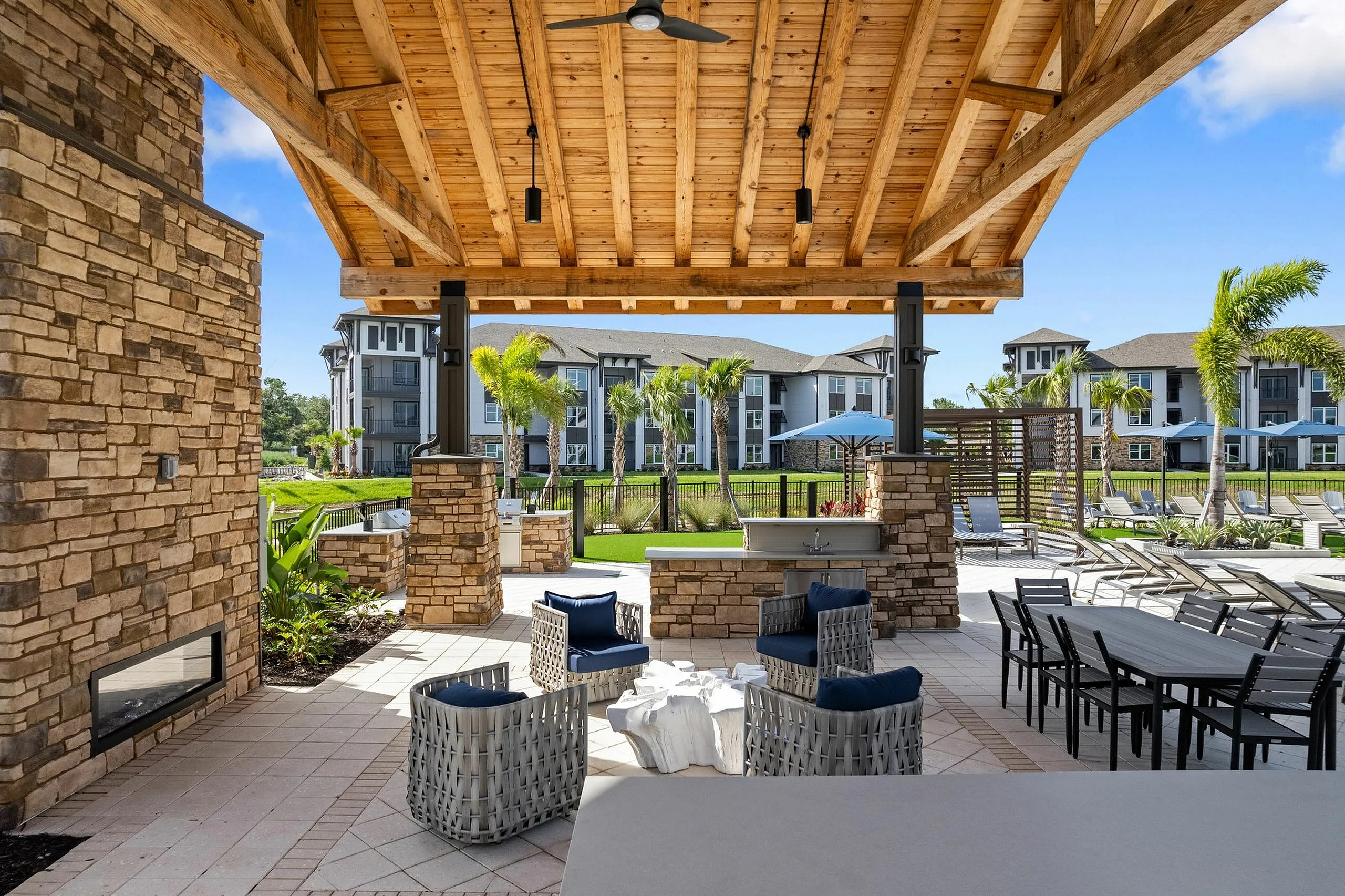 Luxurious outdoor patio with stylish seating areas, wooden pergola, and inviting view of modern apartments surrounded by lush greenery.