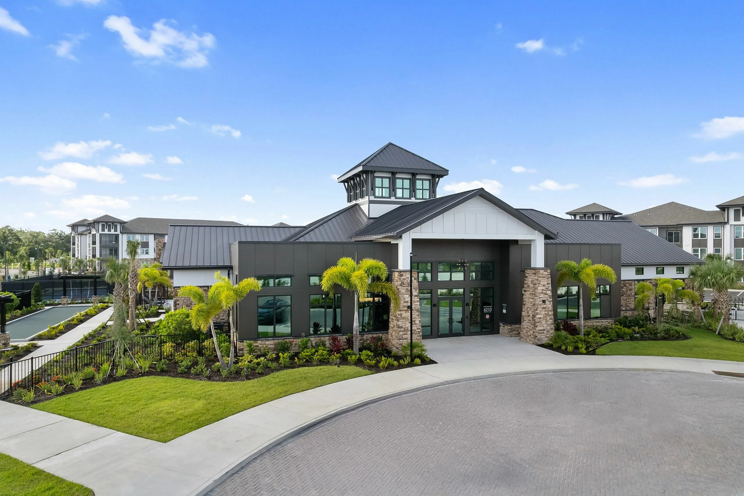 Elegant apartment complex exterior showcasing modern architecture, lush landscaping, and vibrant palm trees under a clear blue sky.