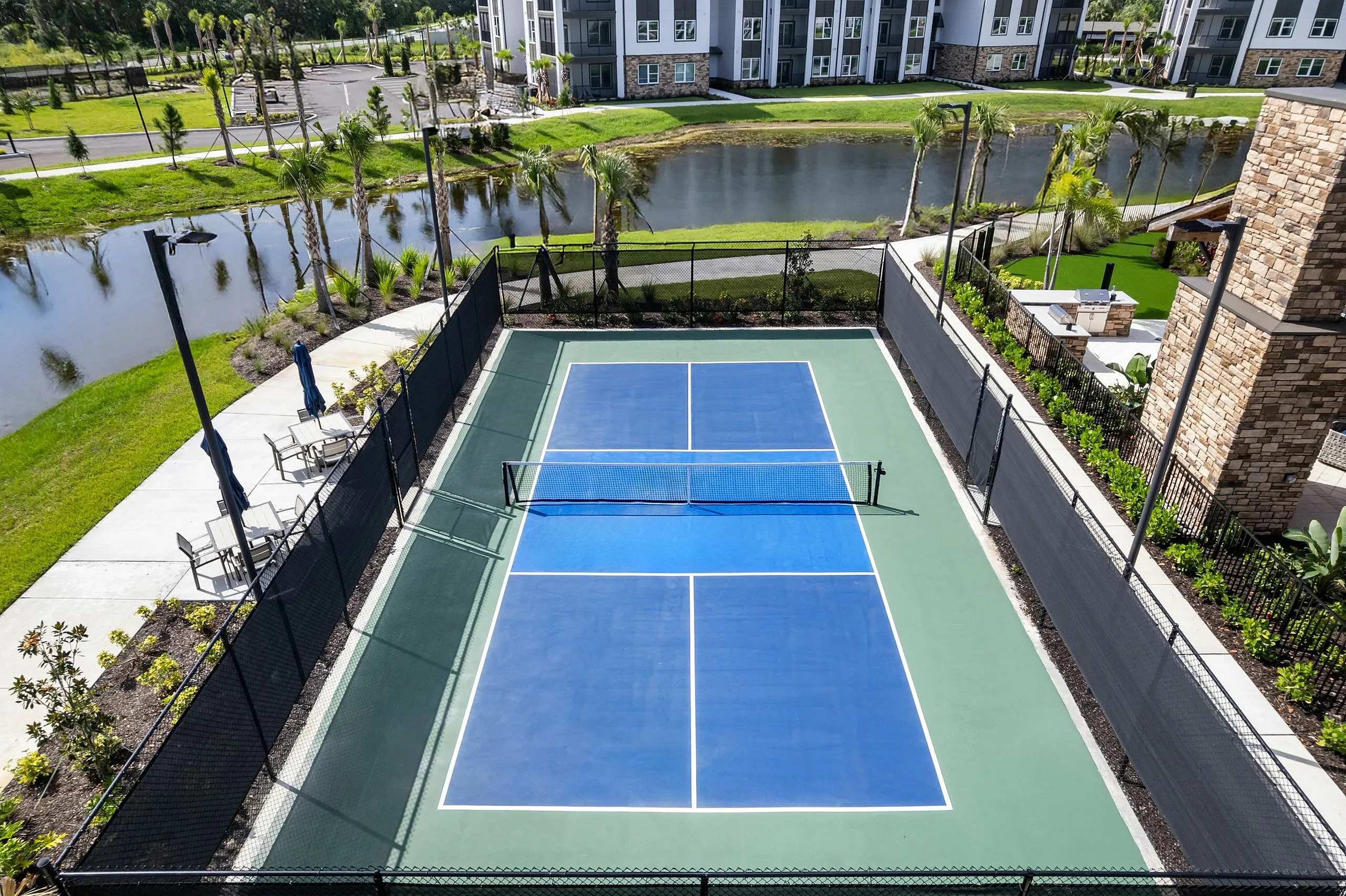 Luxurious apartment complex featuring a pristine tennis court surrounded by lush greenery and serene water views, perfect for active living.
