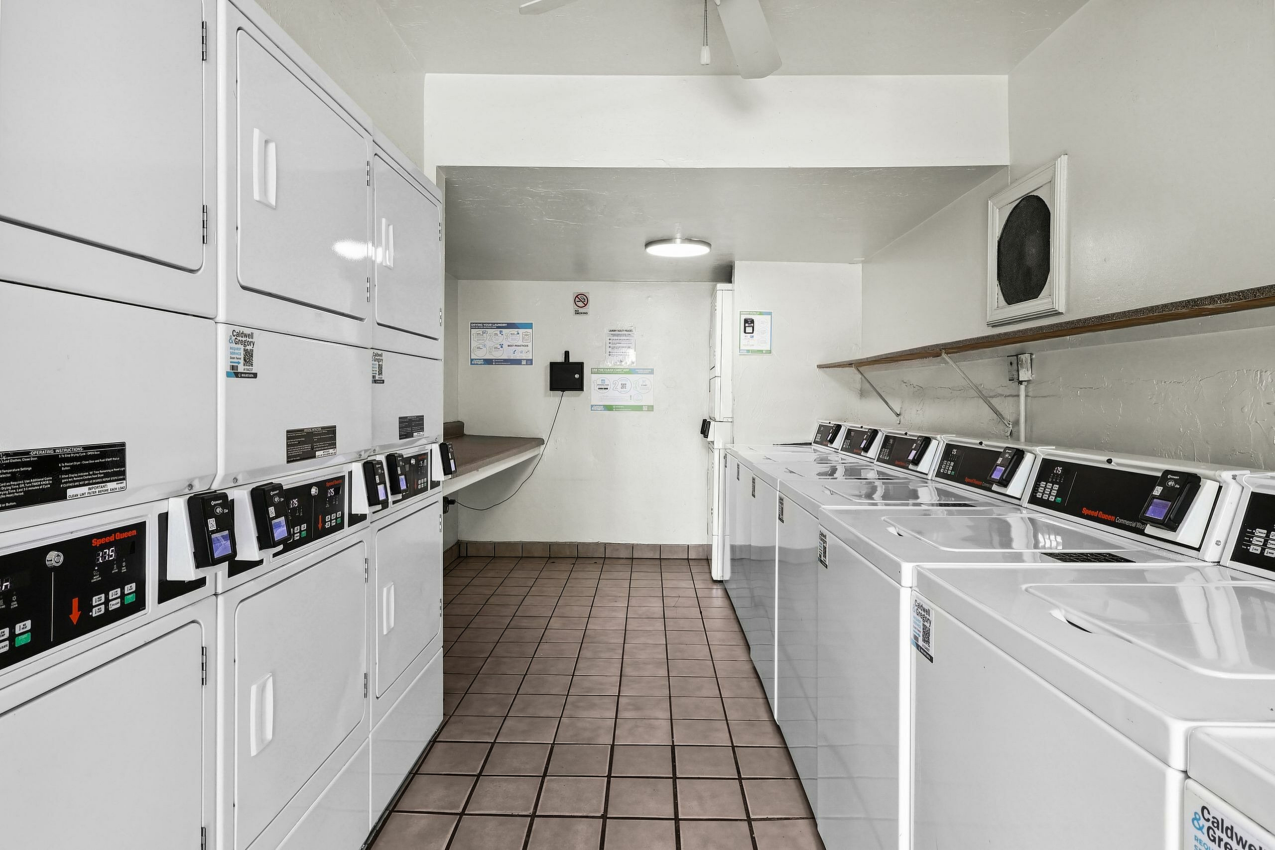Modern laundry room with stacks of efficient washers and dryers, pristine tile flooring, and ample folding space.