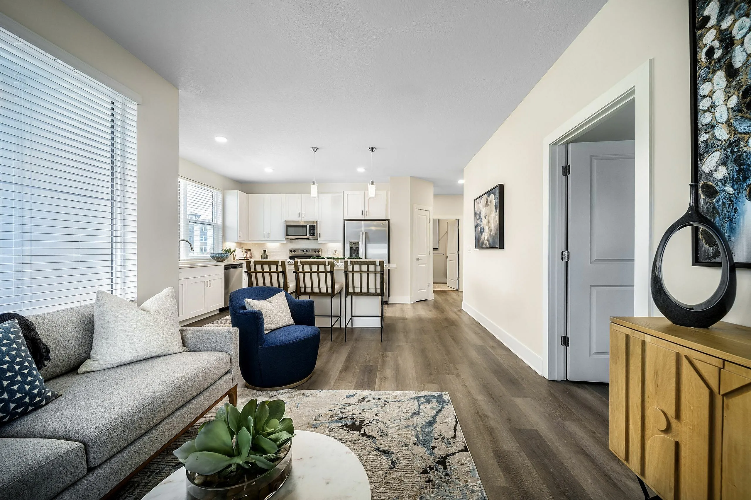 Modern apartment living area with elegant hardwood floors, cozy gray sofa, and stylish open-plan kitchen with white cabinetry.