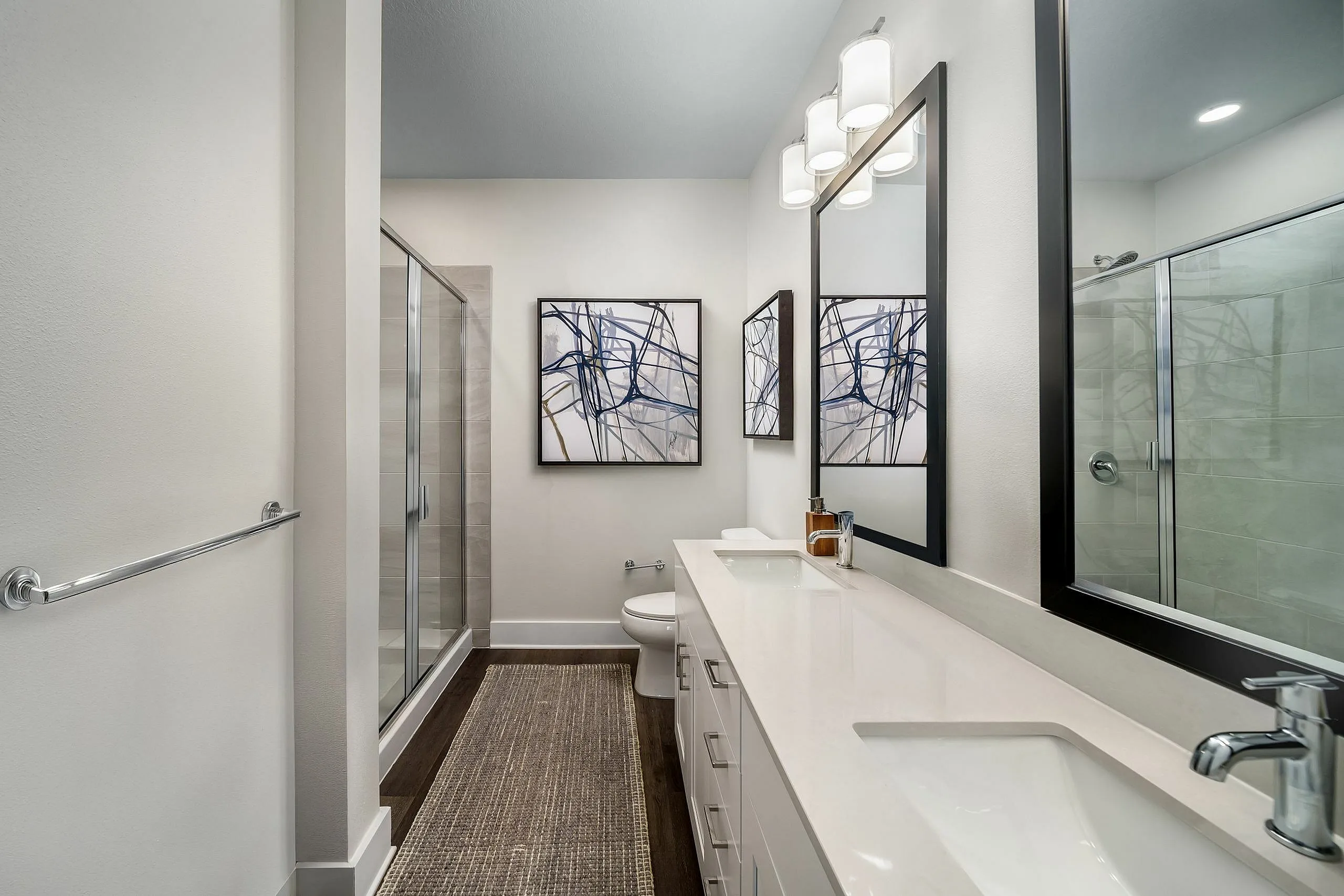 Modern bathroom with sleek double sinks, large mirrors, glass-enclosed shower, and abstract artwork on the walls.