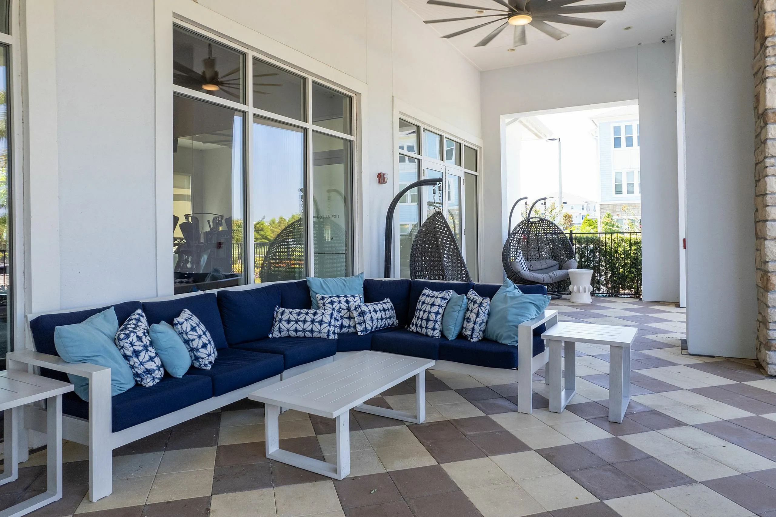 Chic outdoor lounge area with stylish navy and white sofas, modern accent pillows, and inviting hanging chairs, perfect for relaxing.