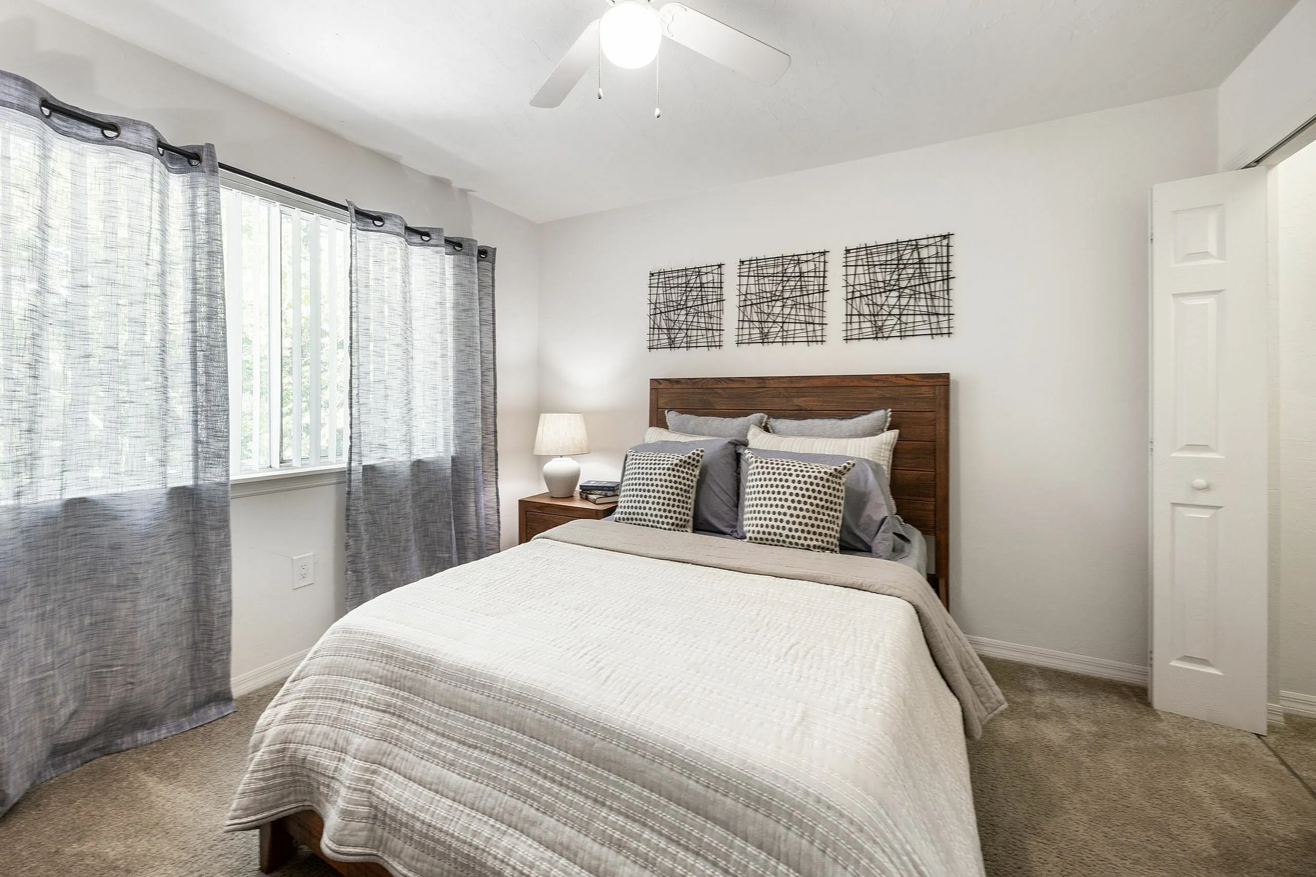 Inviting bedroom with a cozy bed, soft lighting, and elegant decor, framed by natural light from large windows and stylish curtains.