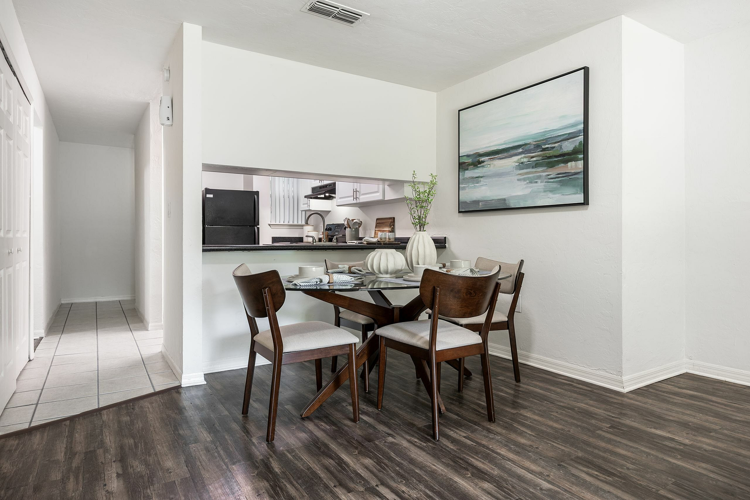 Chic dining area with elegant wooden furniture, hardwood floors, and a modern painting, adjacent to a sleek open kitchen with contemporary appliances.