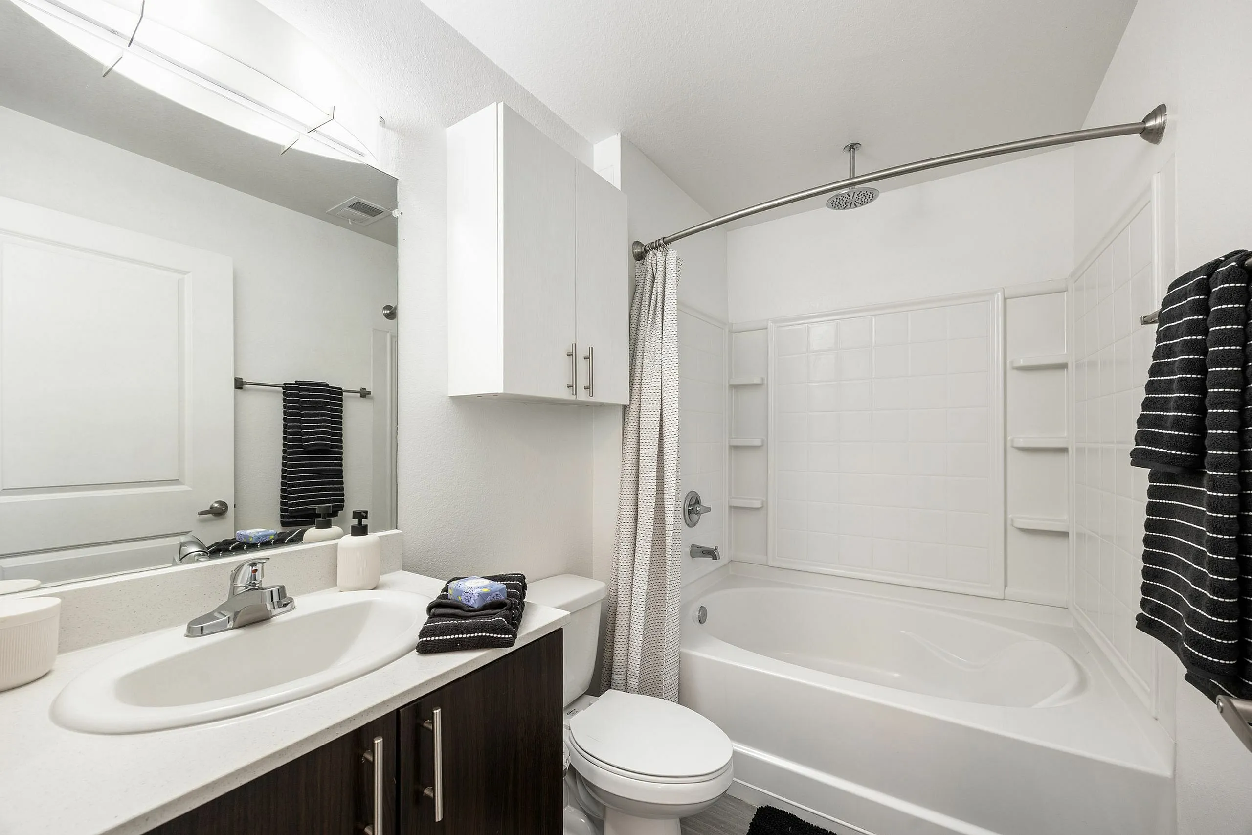 Modern, bright bathroom featuring a sleek countertop sink, elegant cabinetry, and a spacious white bathtub with a curved shower rod.