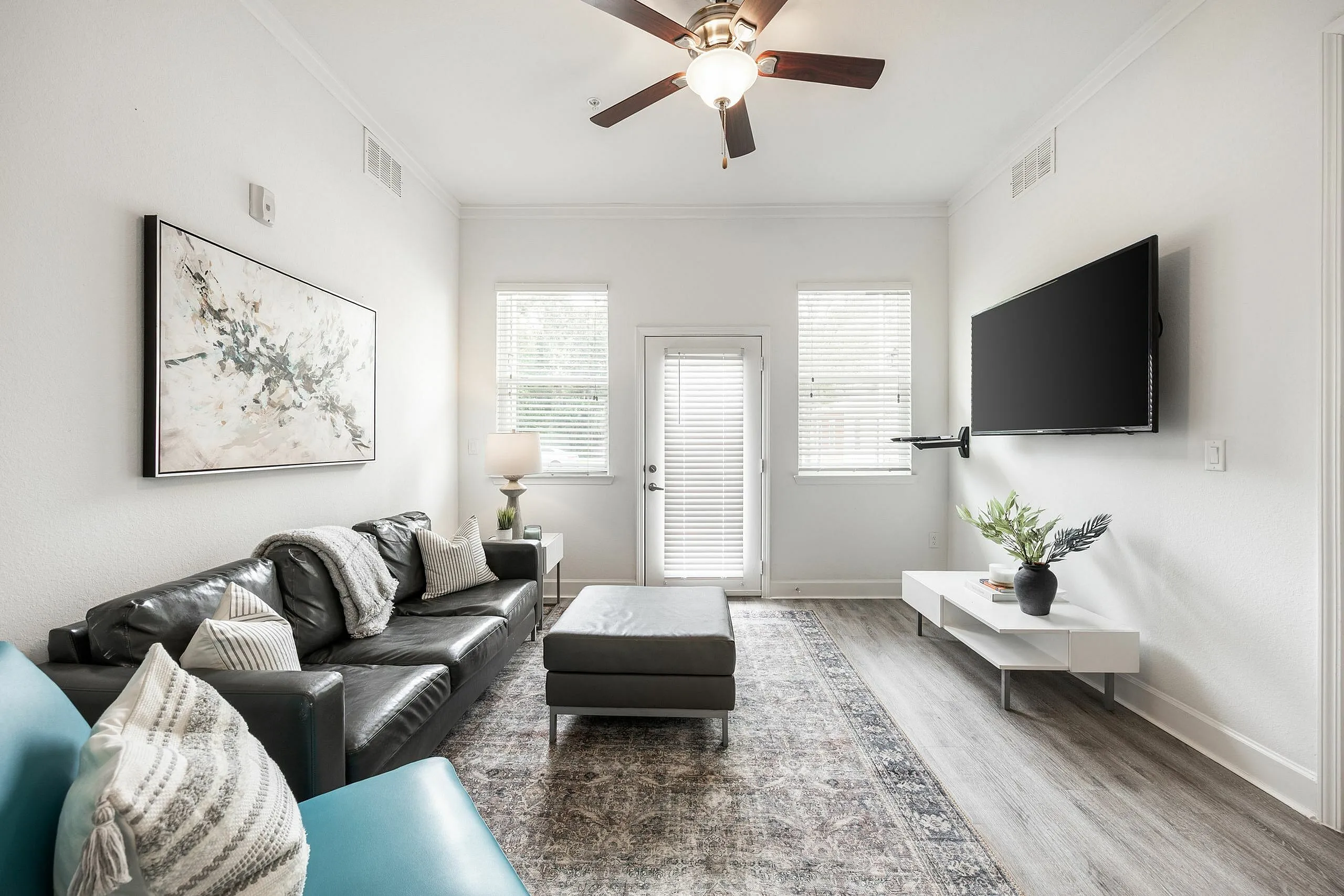 Chic and airy living room with modern decor, large leather sofa, wall-mounted TV, and elegant ceiling fan, perfect for relaxation.