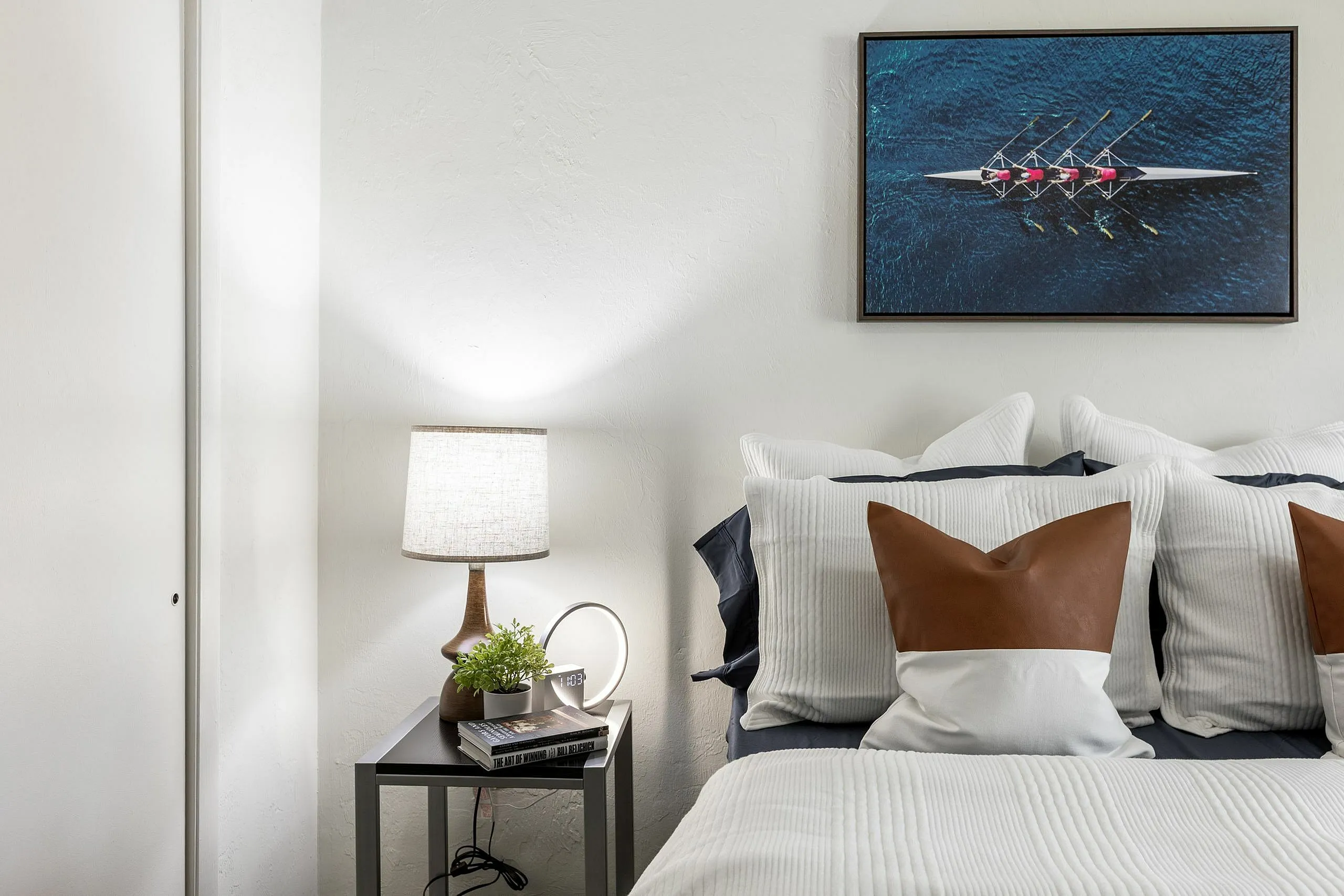 Elegant bedroom scene showcasing plush pillows, a chic table lamp, and modern art, creating a cozy and inviting atmosphere.