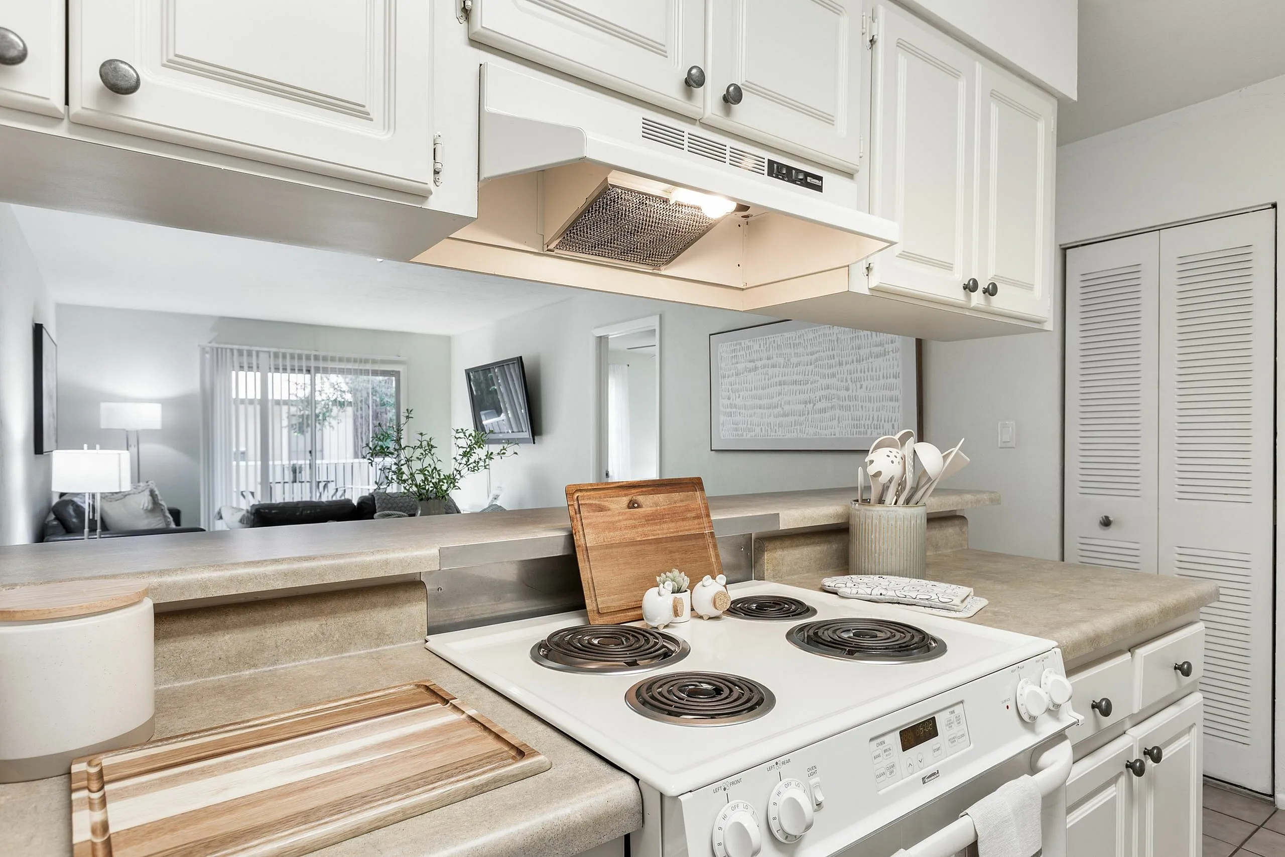 Bright and airy kitchen with sleek countertops leading to a cozy living room, featuring modern decor and abundant natural light.