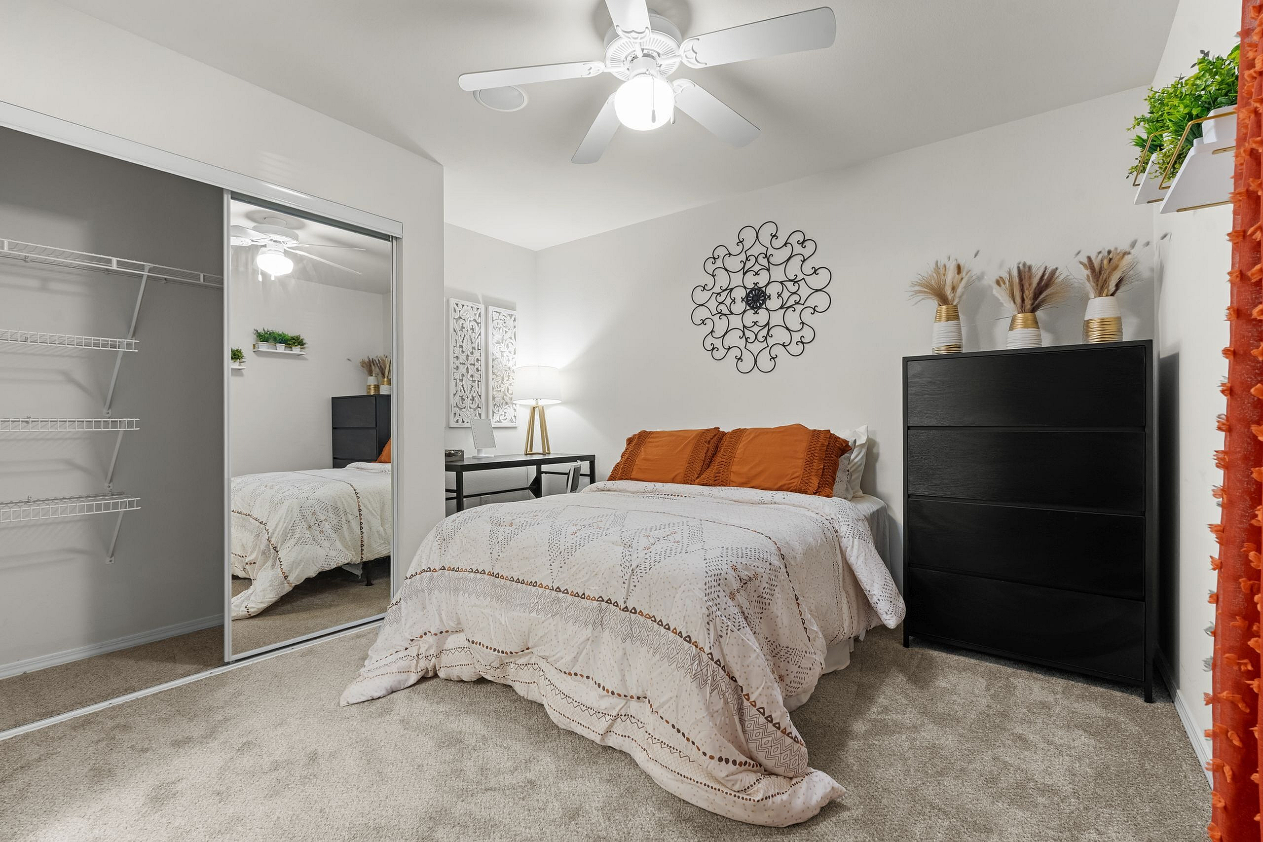 Chic bedroom with cozy bedding, vibrant orange pillows, elegant decor, and spacious mirrored closet in a modern apartment.