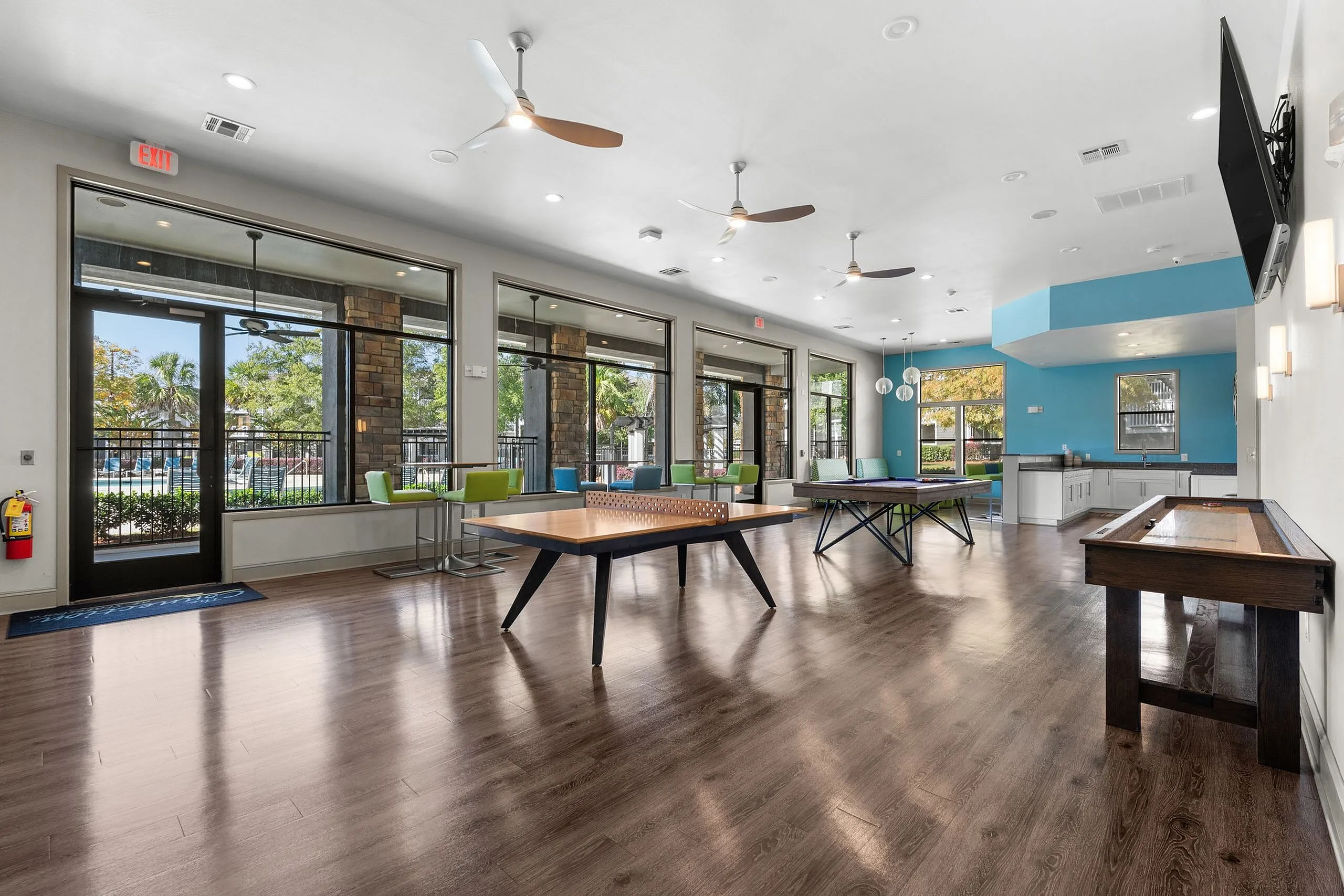 Inviting recreation room with modern design featuring table tennis, shuffleboard, and vibrant seating, overlooking lush greenery and a swimming pool.