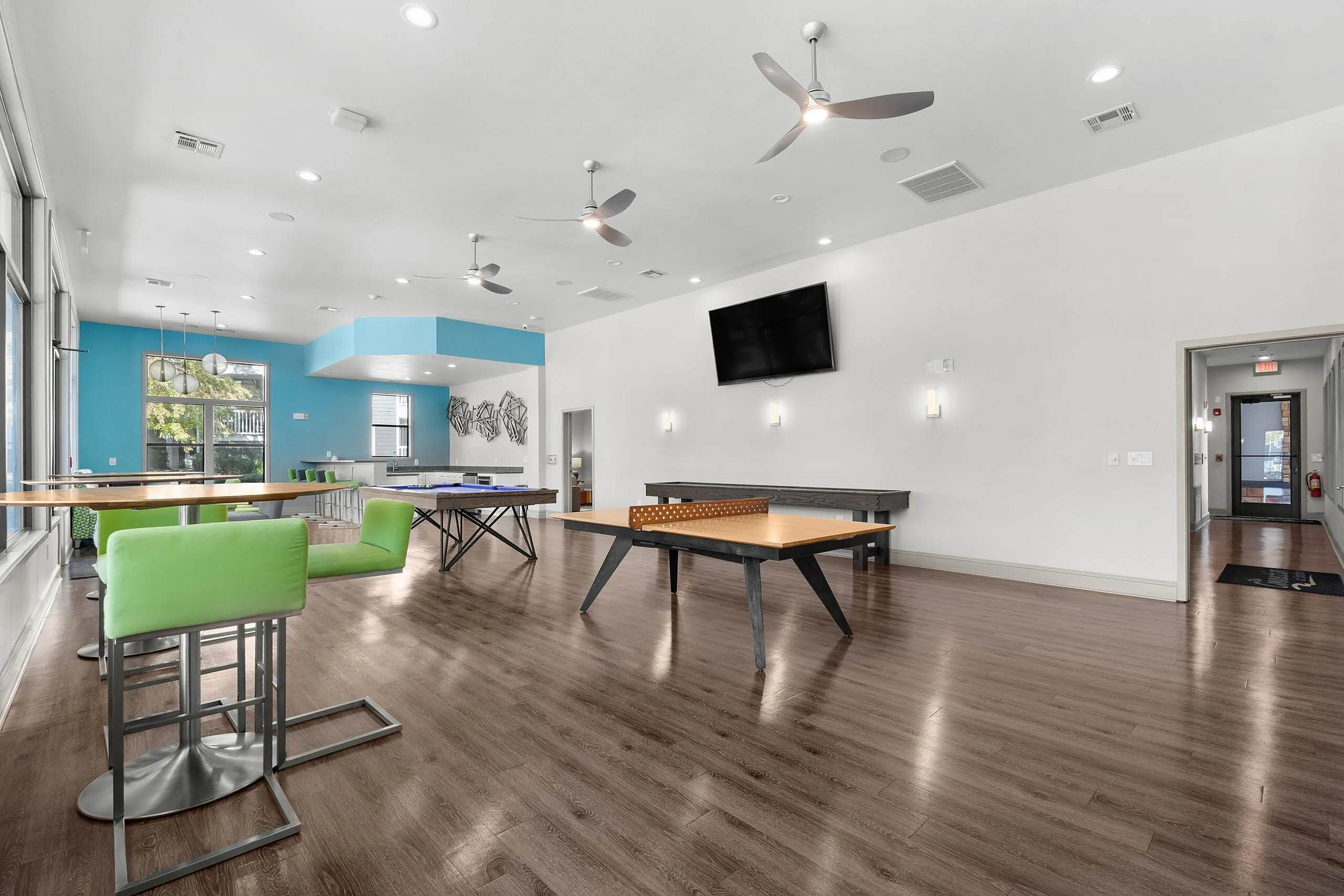 Modern community space featuring sleek wood floors, vibrant green seating, and table tennis setups for entertainment.