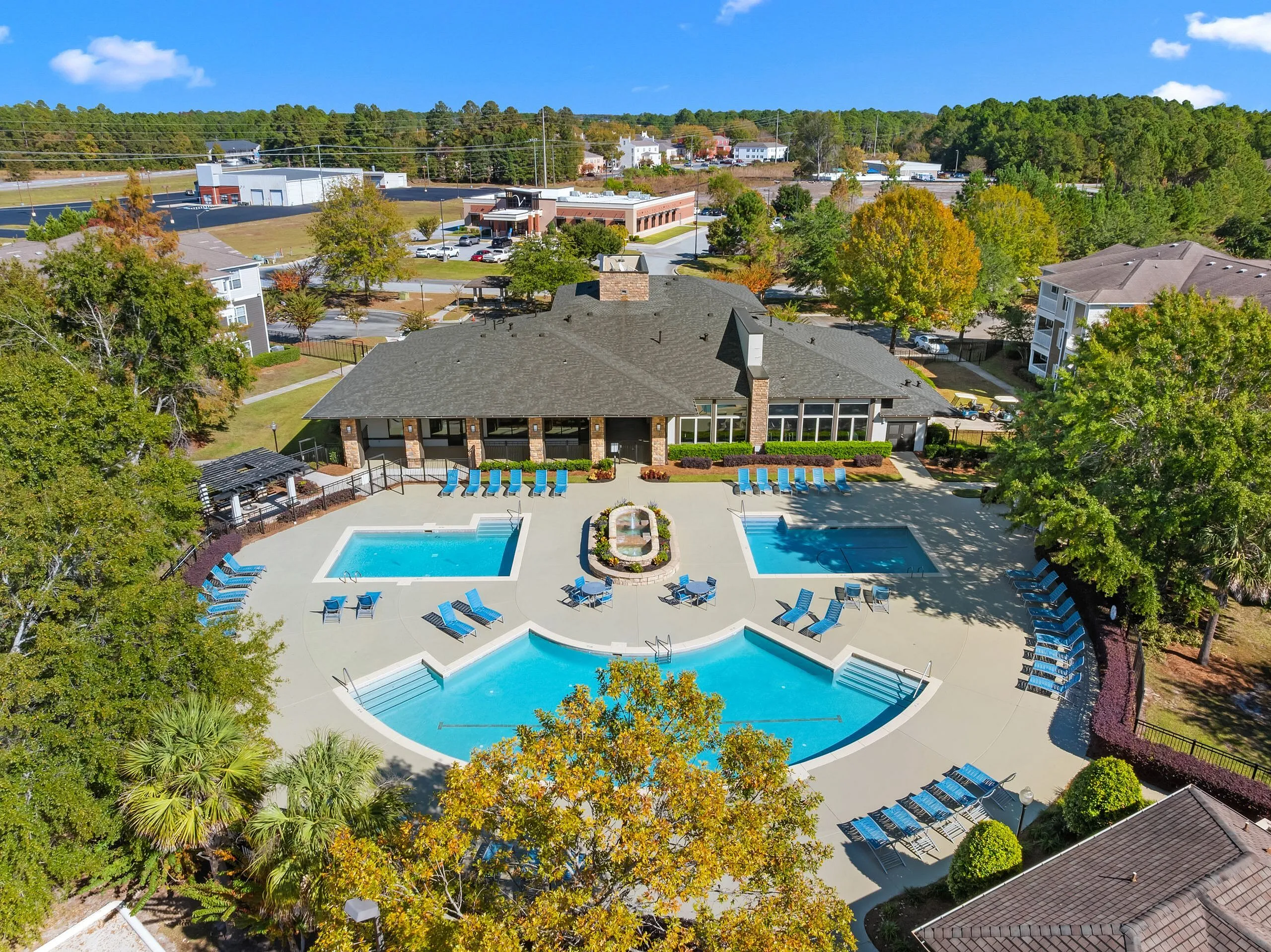 Elegant aerial view of a luxurious apartment complex featuring multiple turquoise swimming pools, surrounded by lush greenery and sun loungers, with residential buildings and vibrant landscaping in the background.