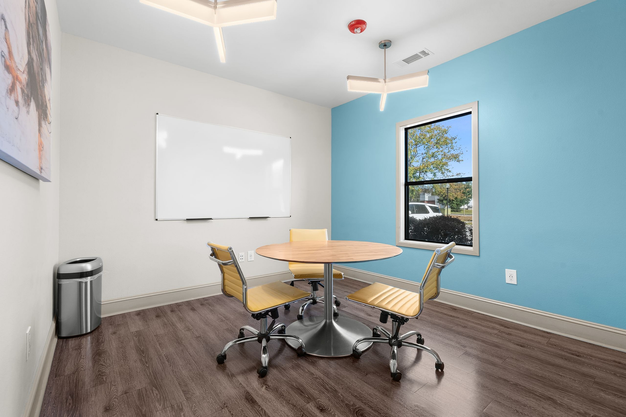Bright and inviting meeting room with modern chairs surrounding a round table, featuring a blue accent wall and large window for natural light.