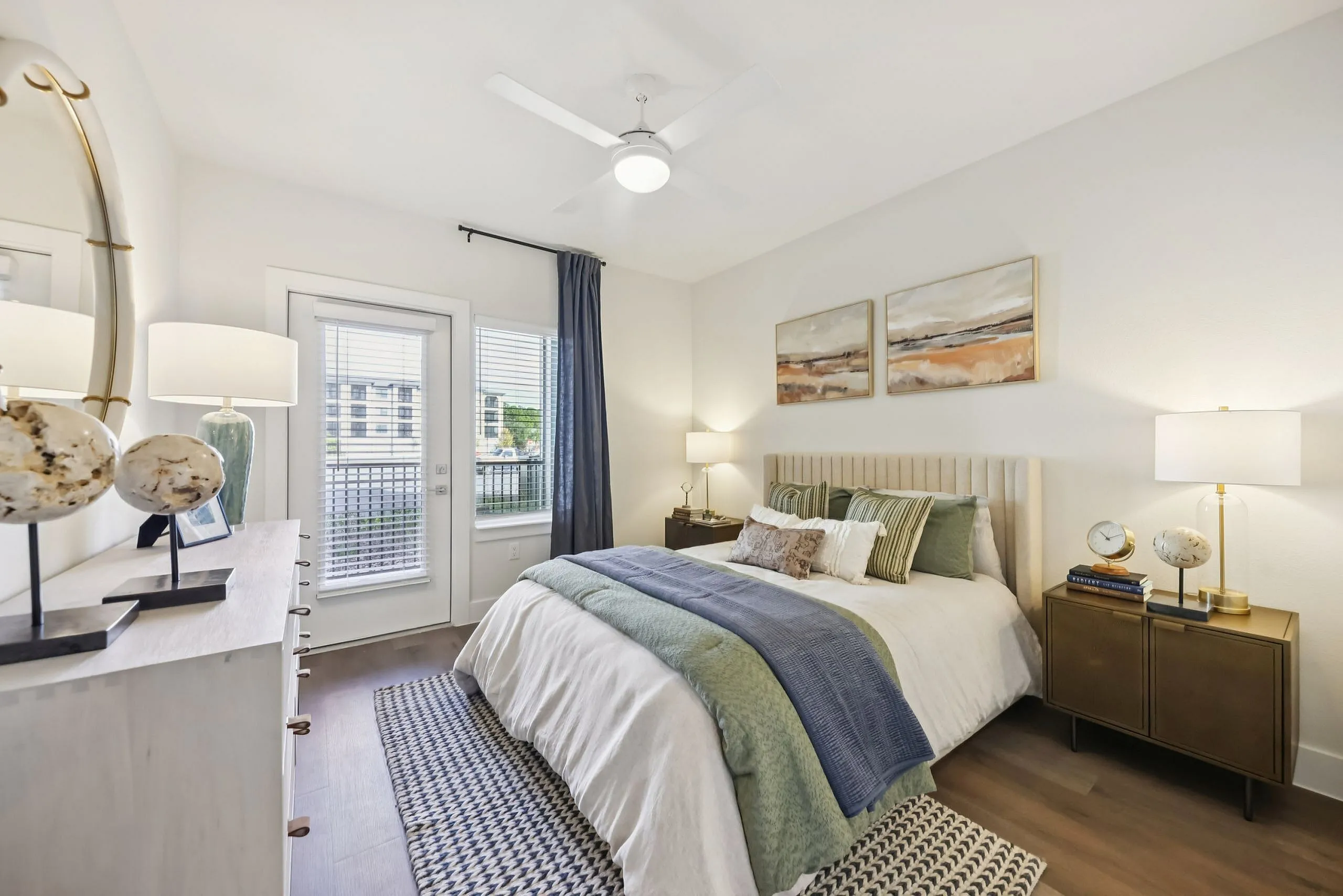 Inviting bedroom with elegant decor, featuring a cozy bed with green accents, modern artwork, and abundant natural light from large windows.