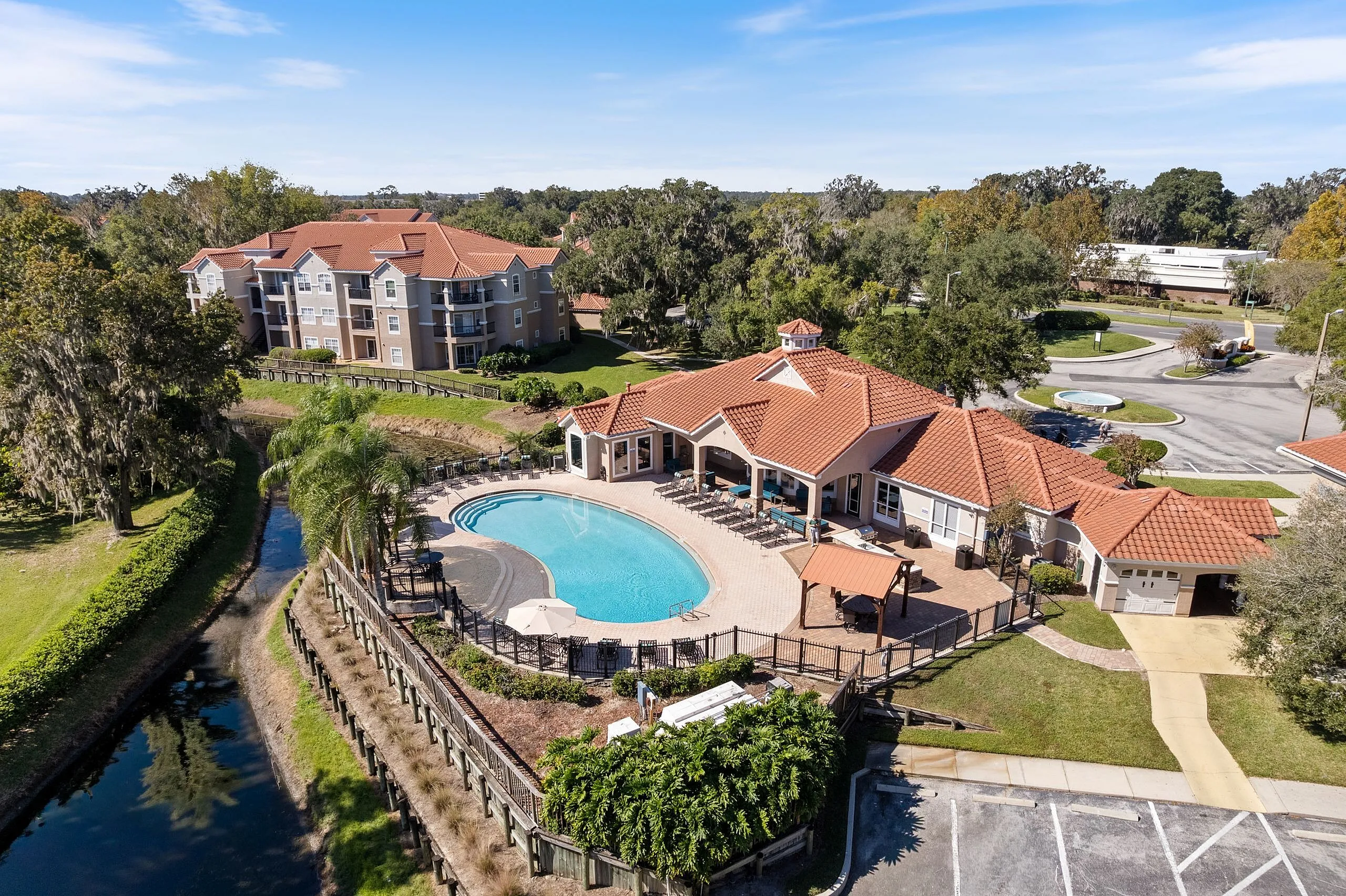 Aerial view of luxurious apartment complex with terracotta roofs, lush landscaping, and inviting swimming pool surrounded by sun loungers and greenery.