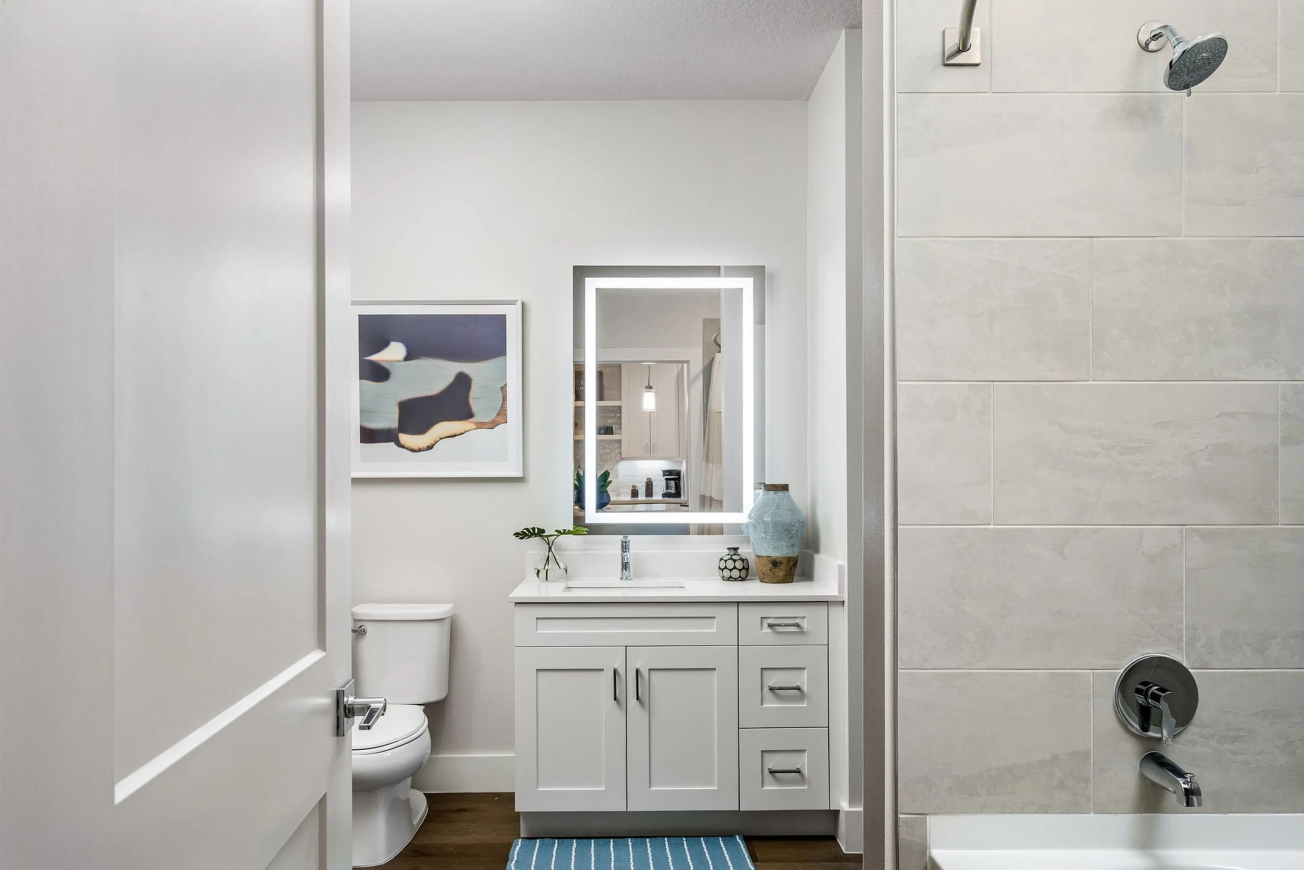 Modern bathroom featuring sleek white cabinetry, elegant wall art, and a luminous mirror, exuding contemporary style.