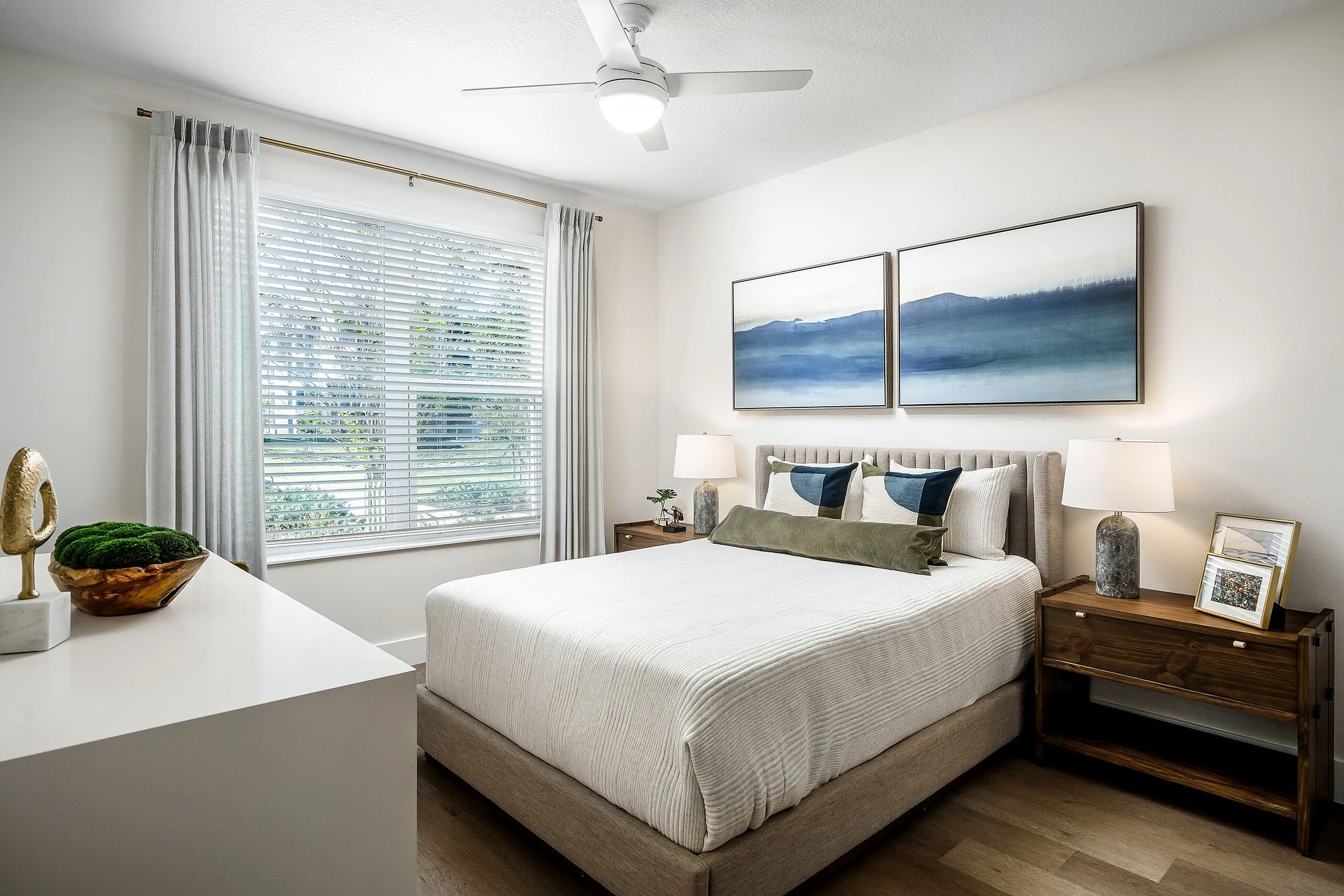 Bright and cozy bedroom with modern decor, featuring large windows, elegant artwork, and stylish wooden furniture.