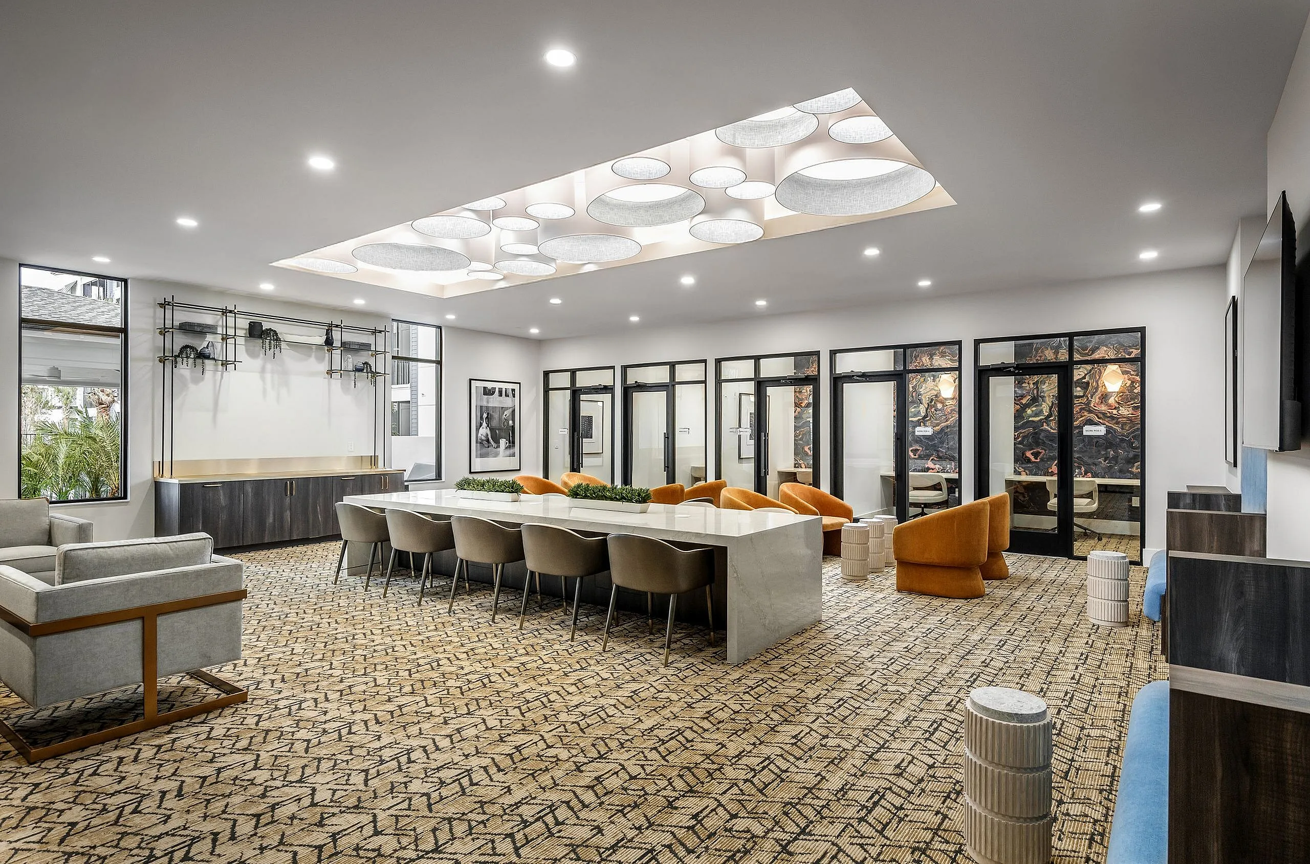 Elegant and spacious apartment community room featuring a sleek marble table, modern lighting, plush seating, and stylish decor.