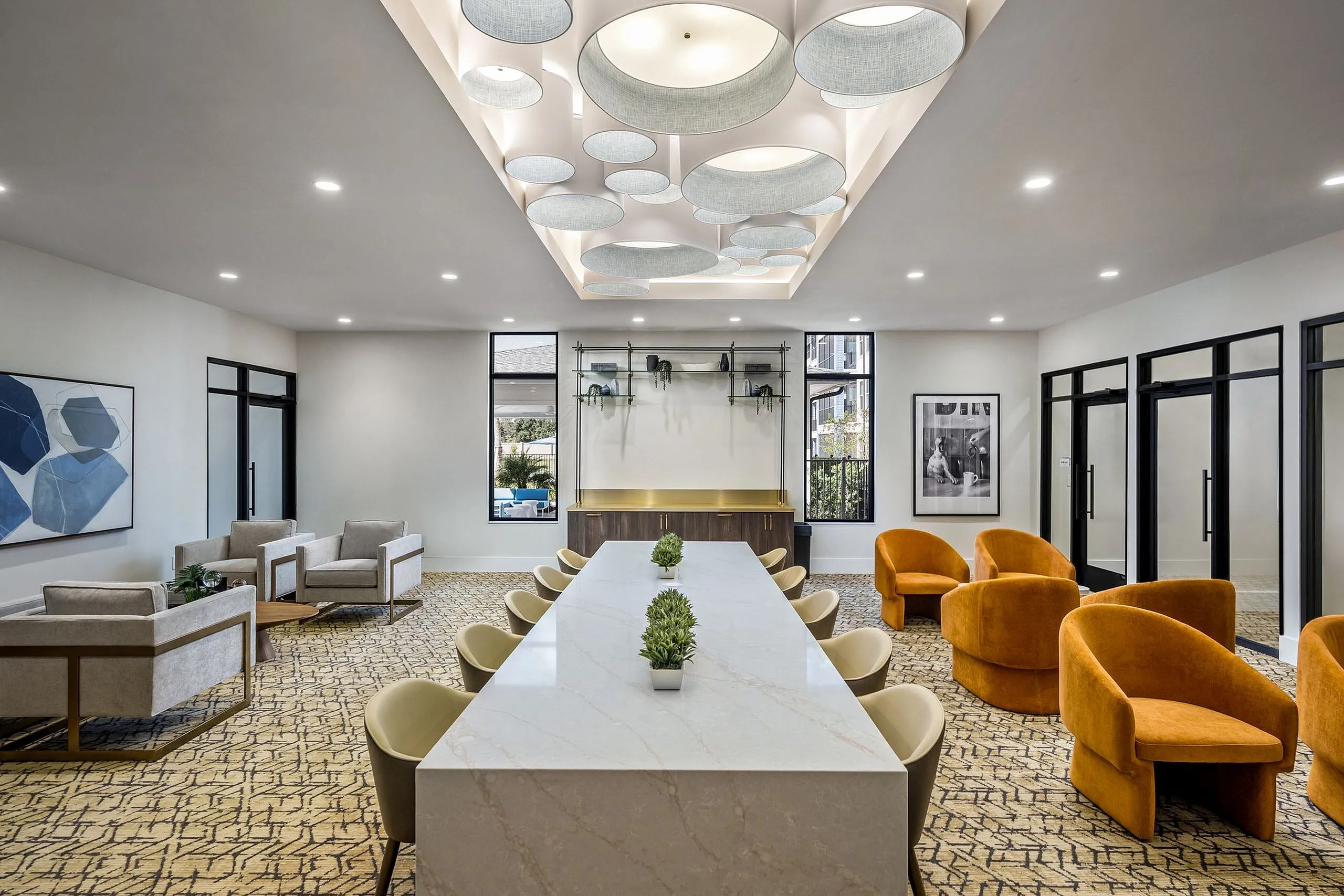 Modern and inviting communal space with elegant seating, a long marble table, and artistic ceiling lights, perfect for meetings or gatherings.