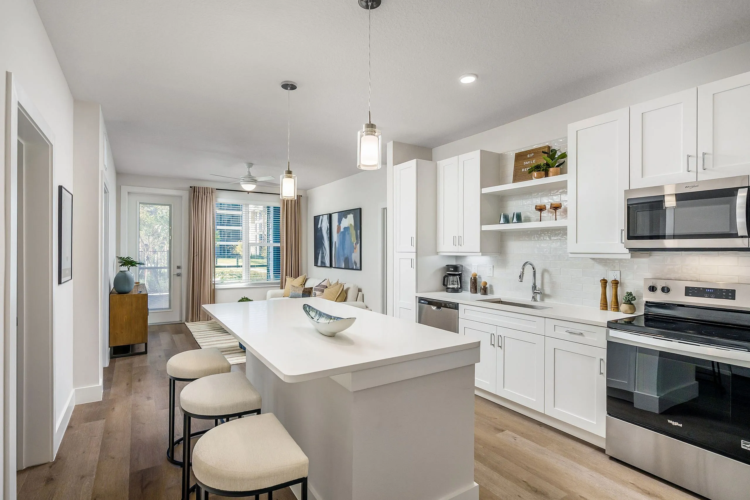 Bright and modern kitchen with sleek white cabinets, stylish island, and cozy seating in an open-concept living space.