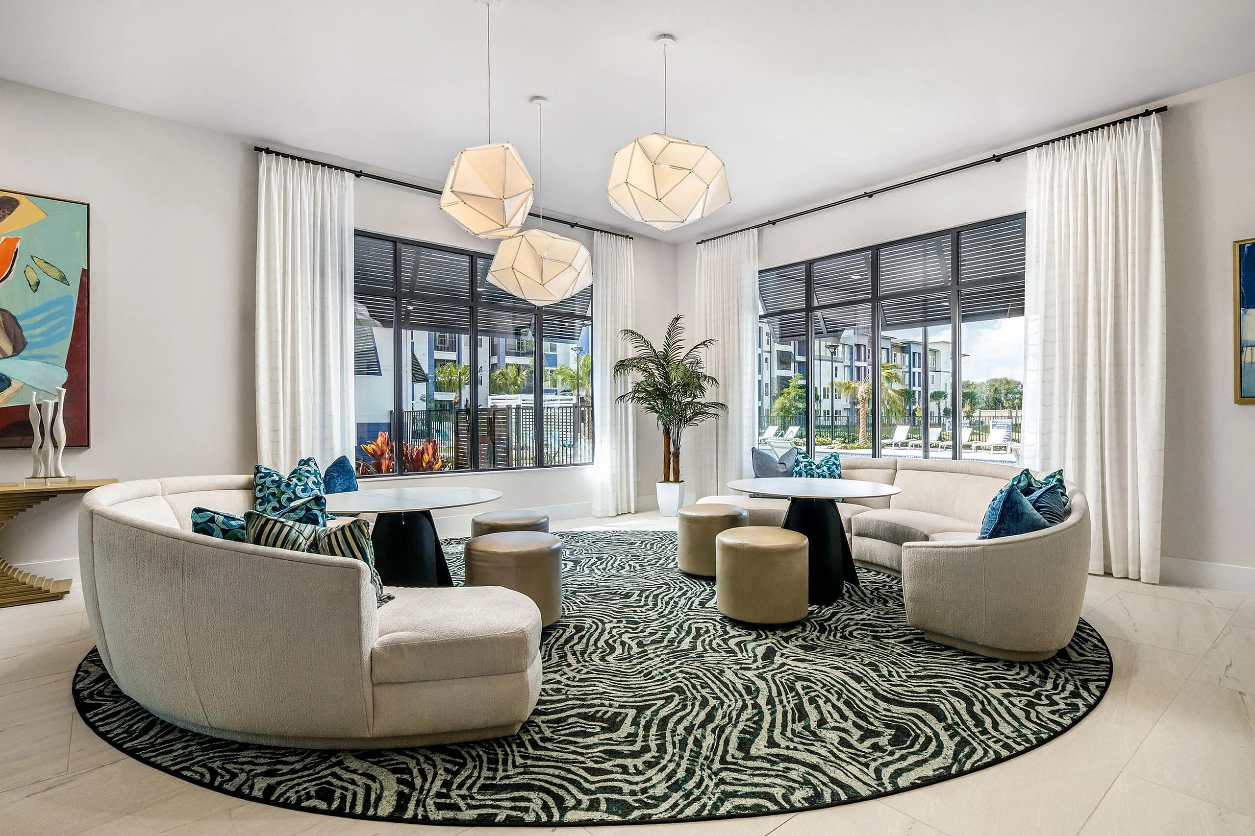 Modern lounge with chic curved sofas, geometric pendant lights, and large windows showcasing a vibrant outdoor view.