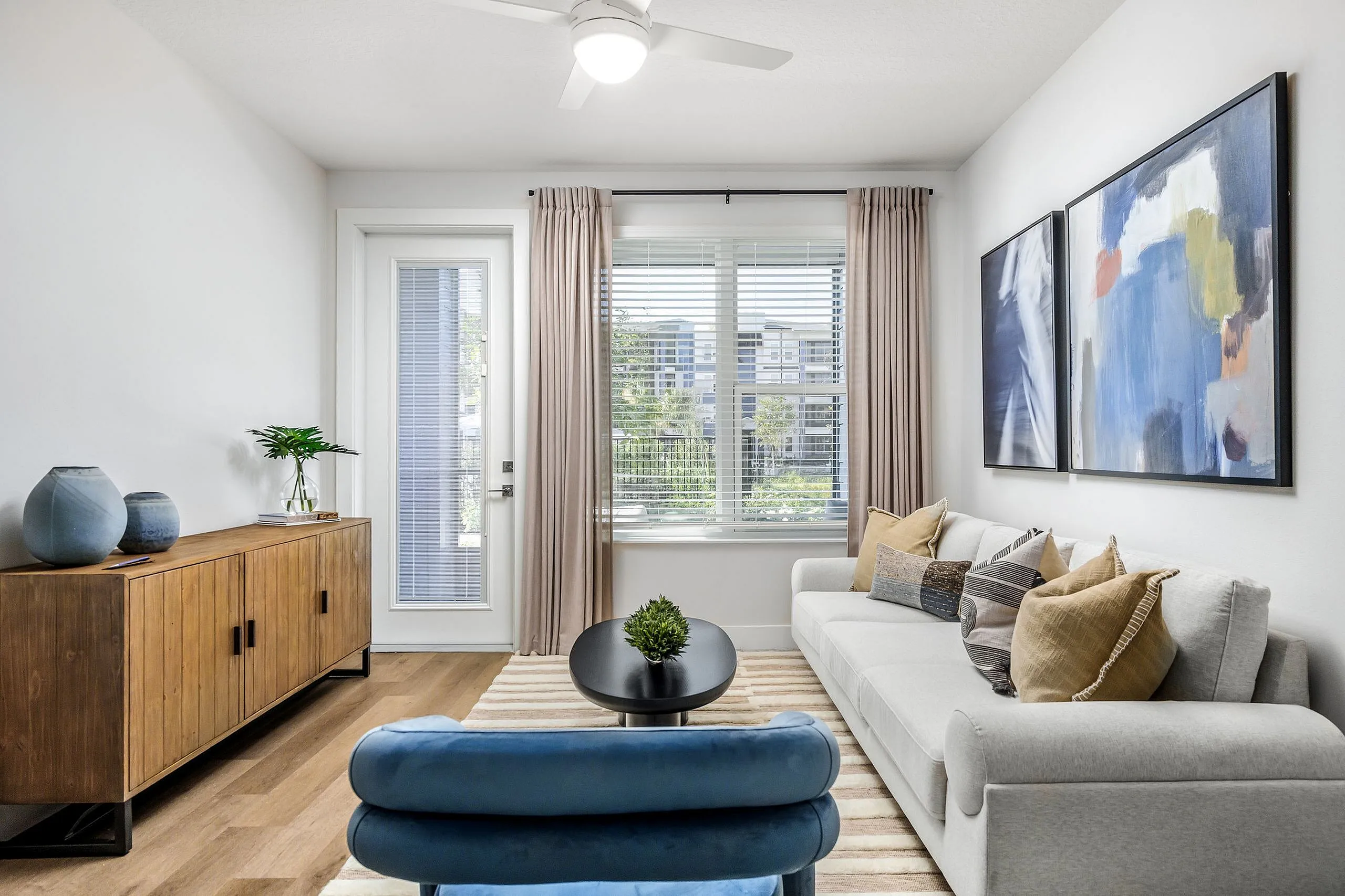Elegant living room with modern decor, featuring a plush white sofa, vibrant abstract art, and a stylish console table beneath a bright window.