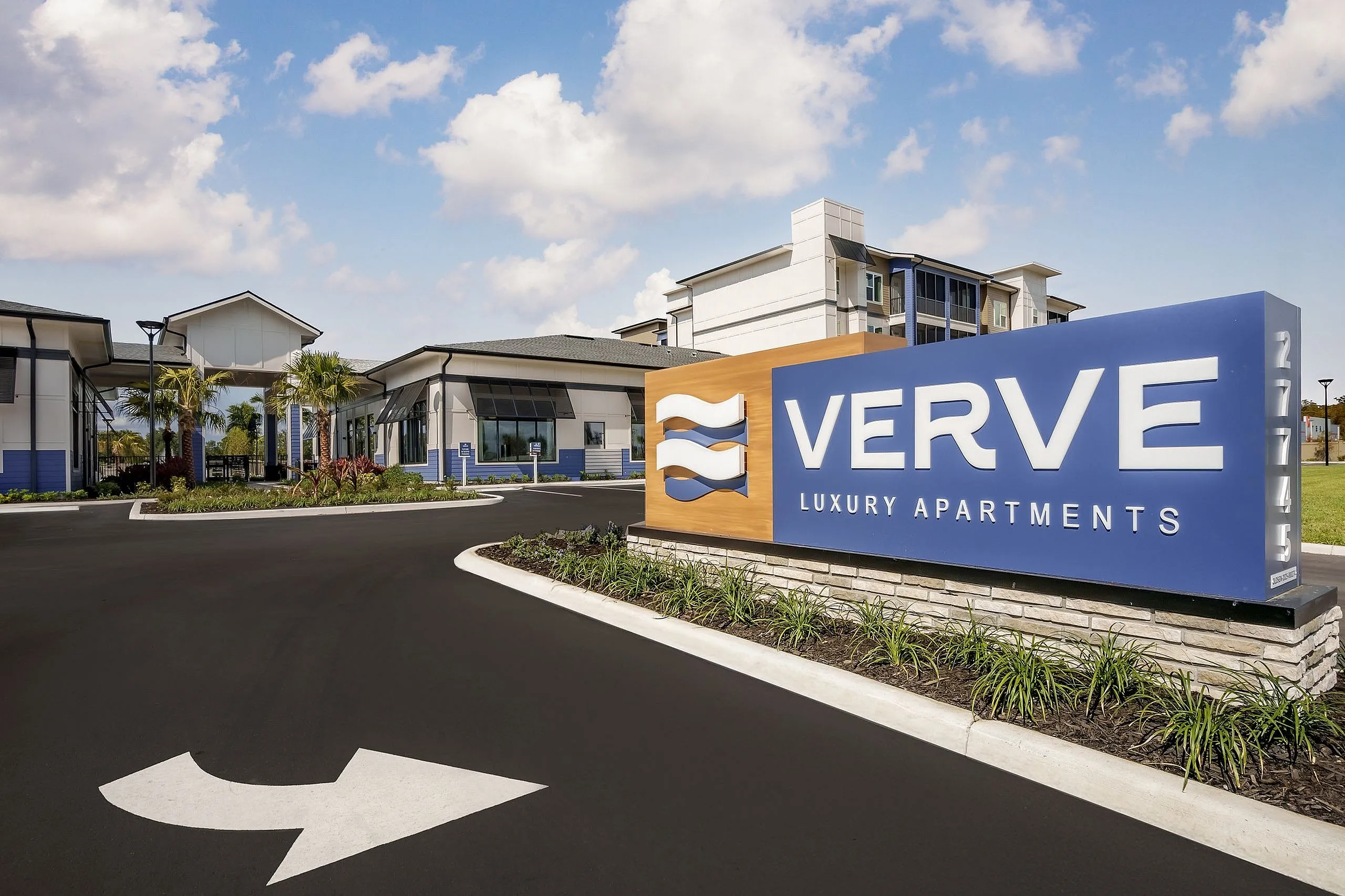 Inviting entrance of Verve Luxury Apartments with modern architecture and lush landscaping under a picturesque sky.