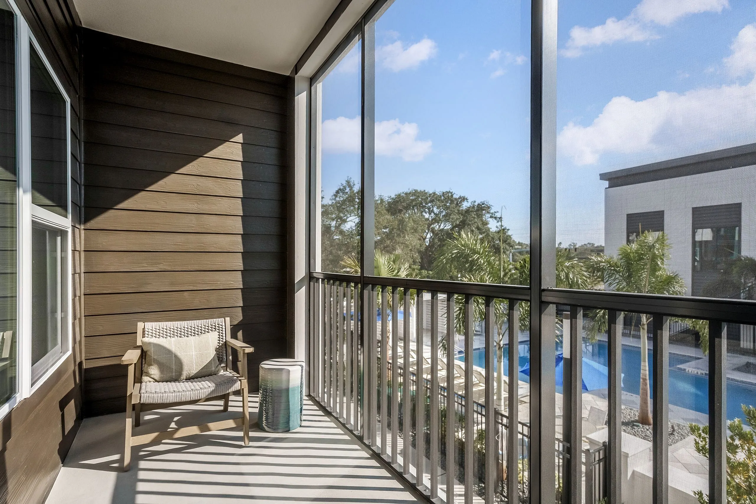 Charming balcony with cozy seating and a view of lush palm trees and a sparkling pool, perfect for relaxing outdoors.