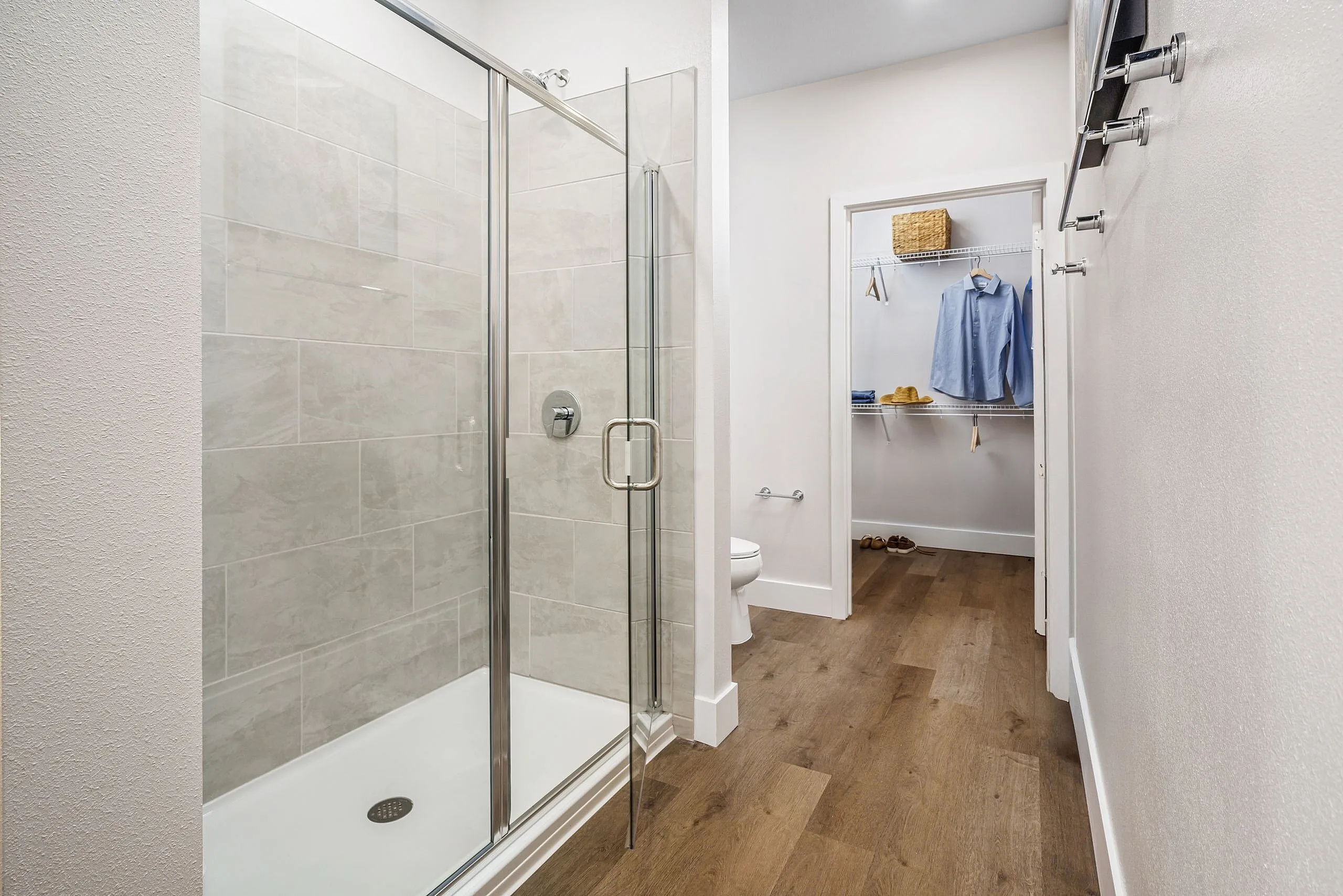 Modern bathroom with elegant glass shower and walk-in closet, featuring stylish wooden flooring and ample natural light.
