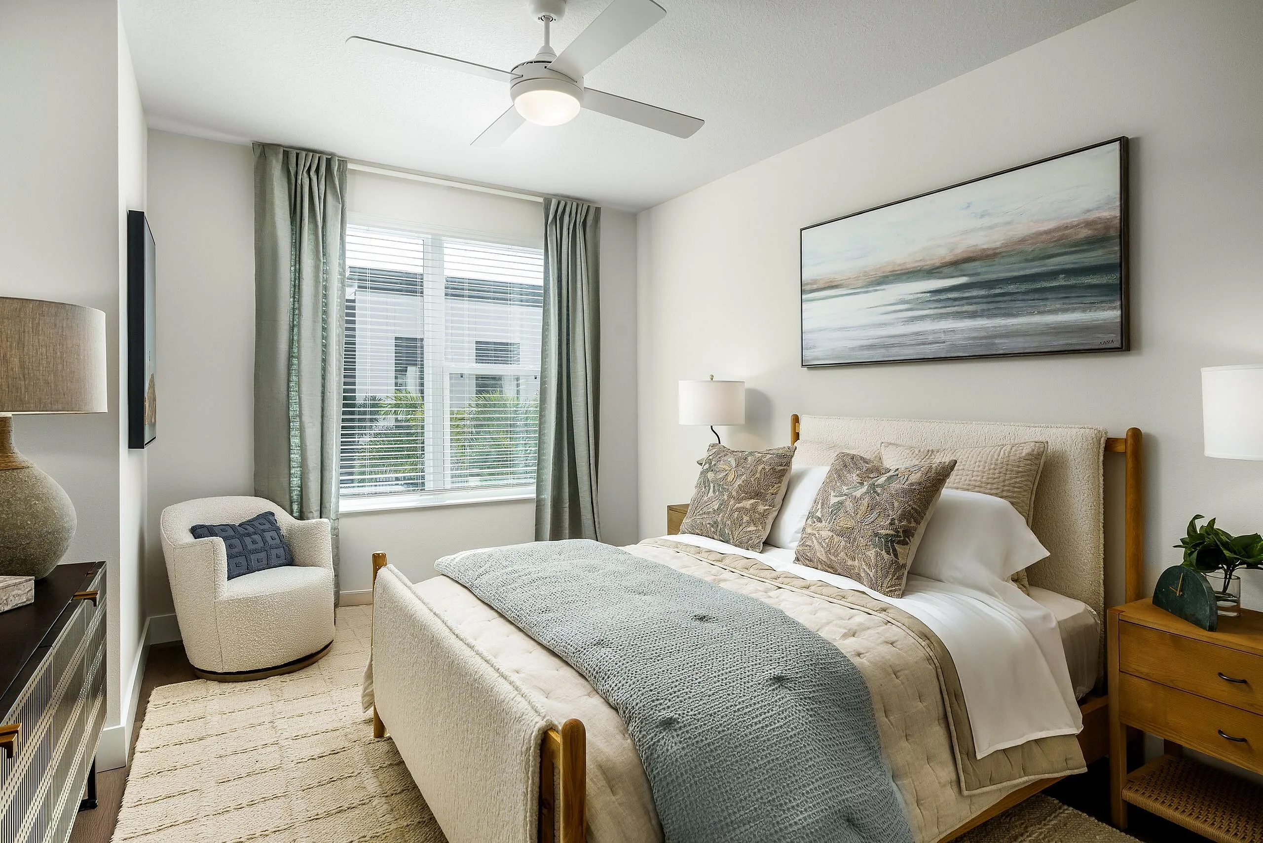 Elegant and serene bedroom with plush bedding, modern fan, and calming artwork, offering a cozy retreat.
