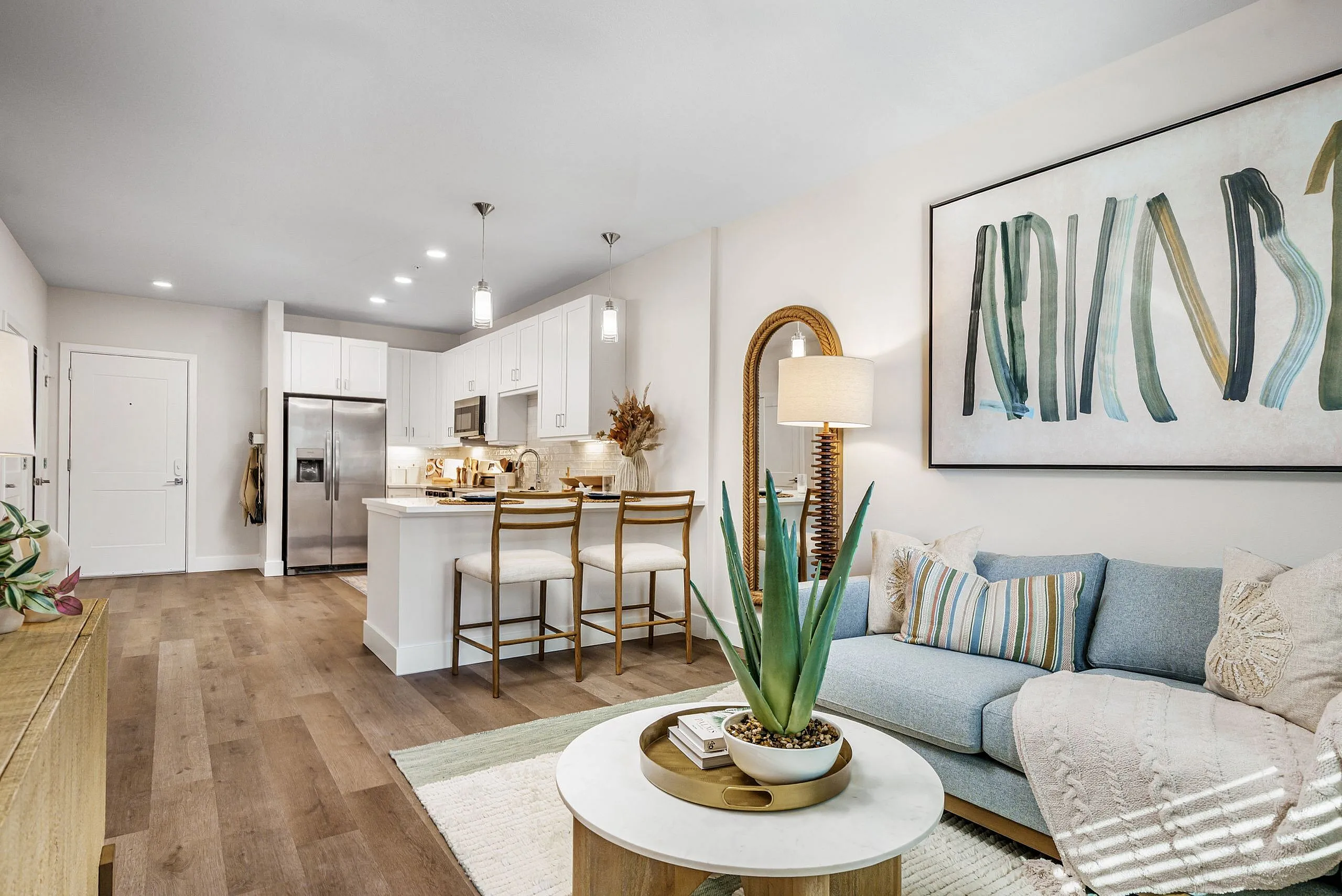 Contemporary open-concept living room with chic decor, cozy sofa, stylish artwork, and modern kitchen featuring sleek appliances and bar seating.