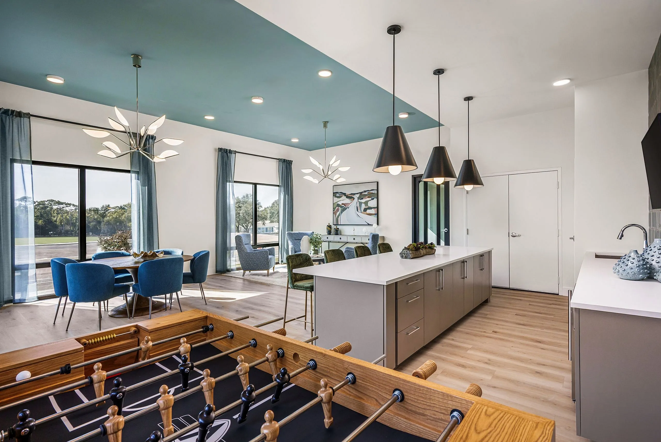 Modern open-concept apartment featuring a stylish kitchen island, chic dining area, and a cozy gaming corner with foosball table.