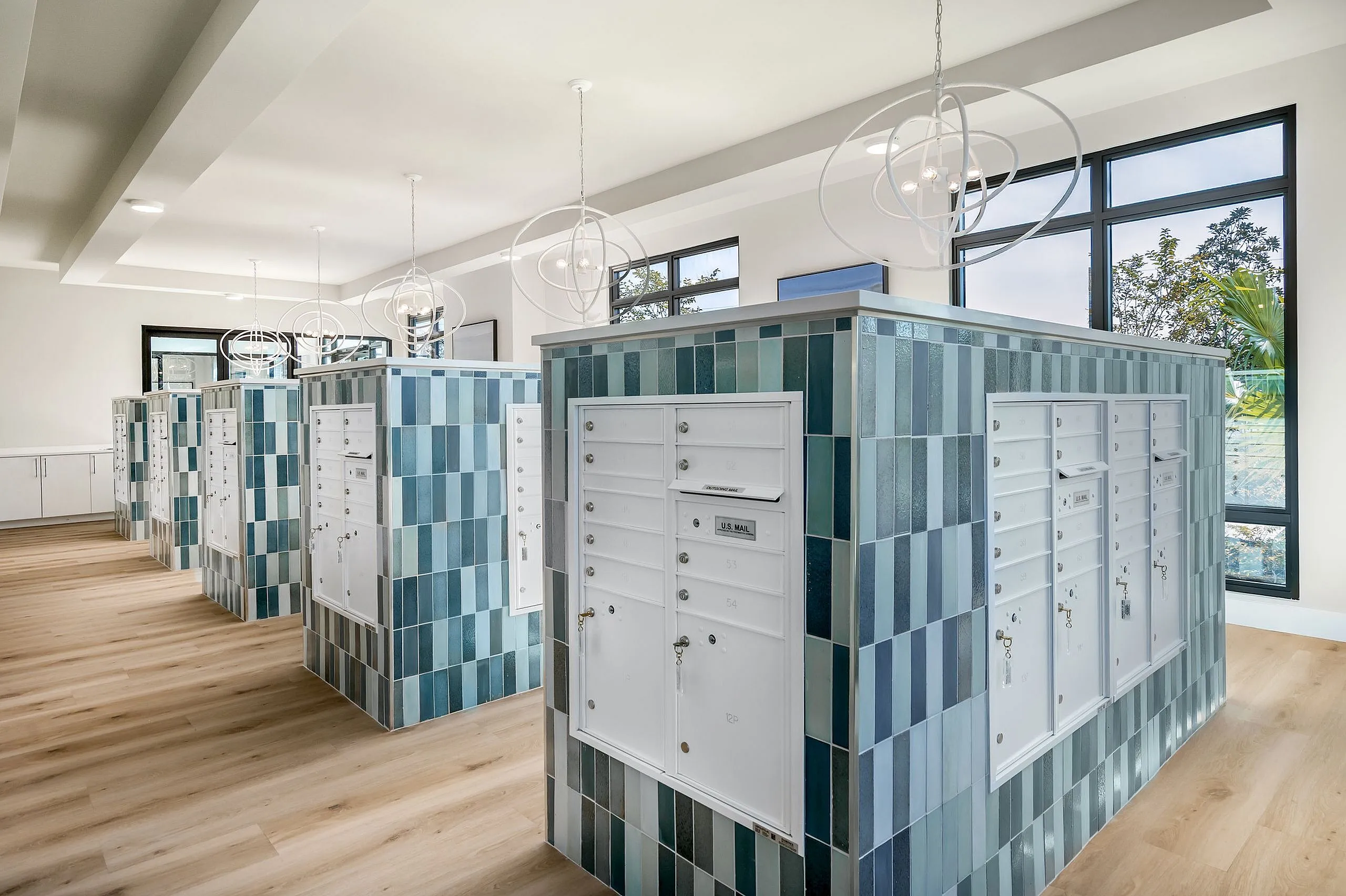 Contemporary mailroom with elegant blue-tiled mailbox units, sleek pendant lighting, and large windows offering natural light.