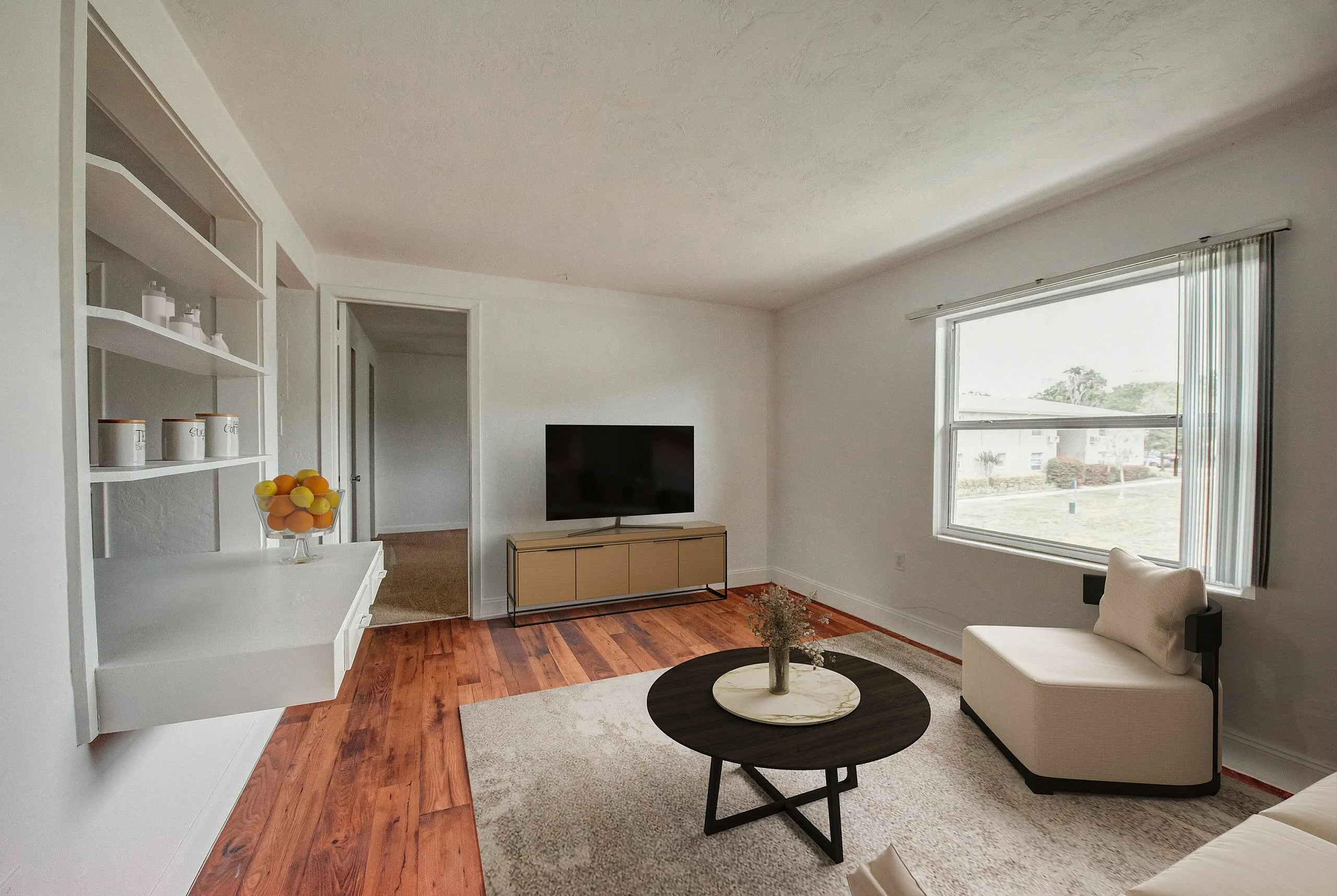 Bright and inviting living room featuring a large window, modern TV setup, and elegant furniture on warm wooden flooring.