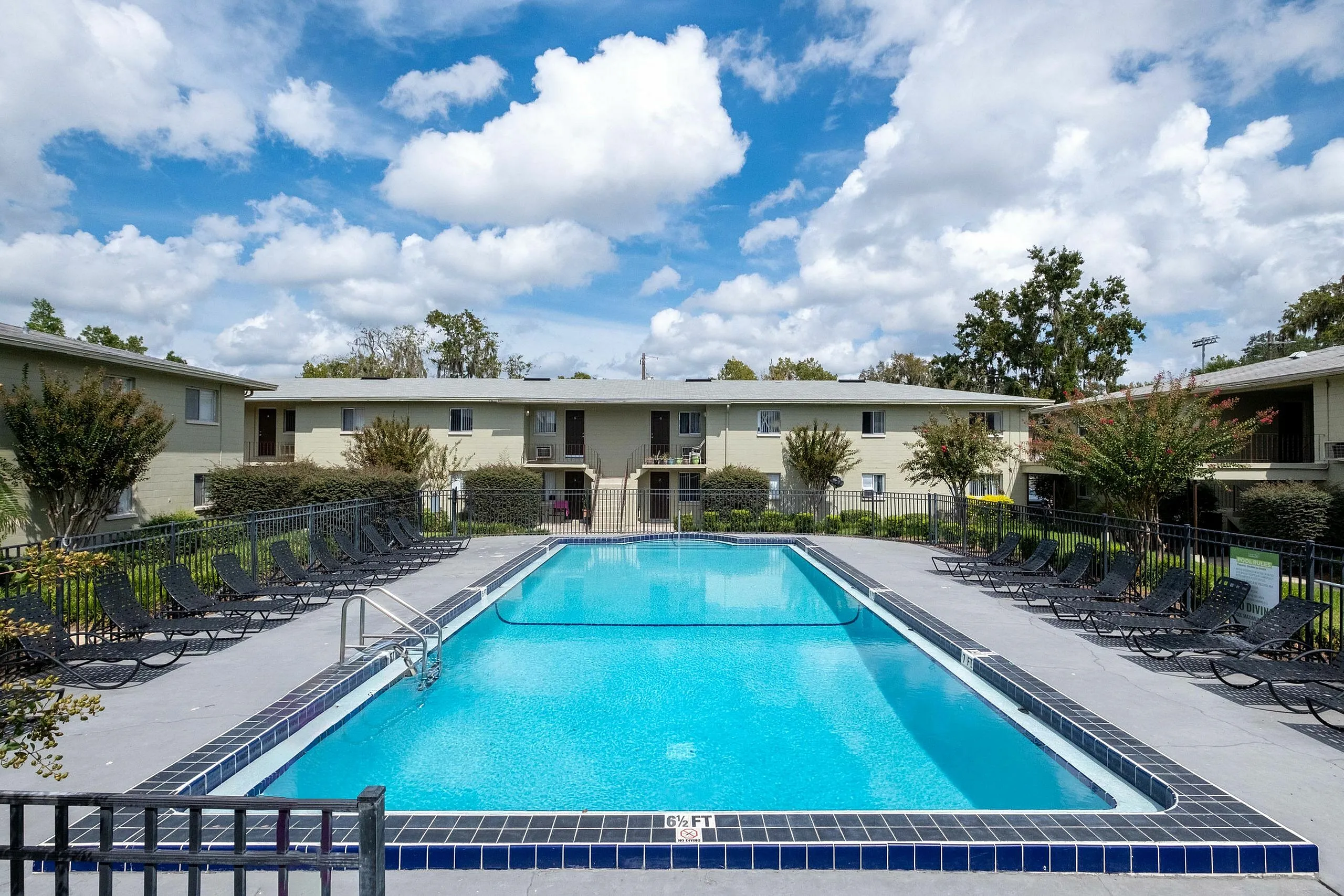 Inviting apartment complex featuring a pristine swimming pool surrounded by sun loungers, under a vibrant blue sky.