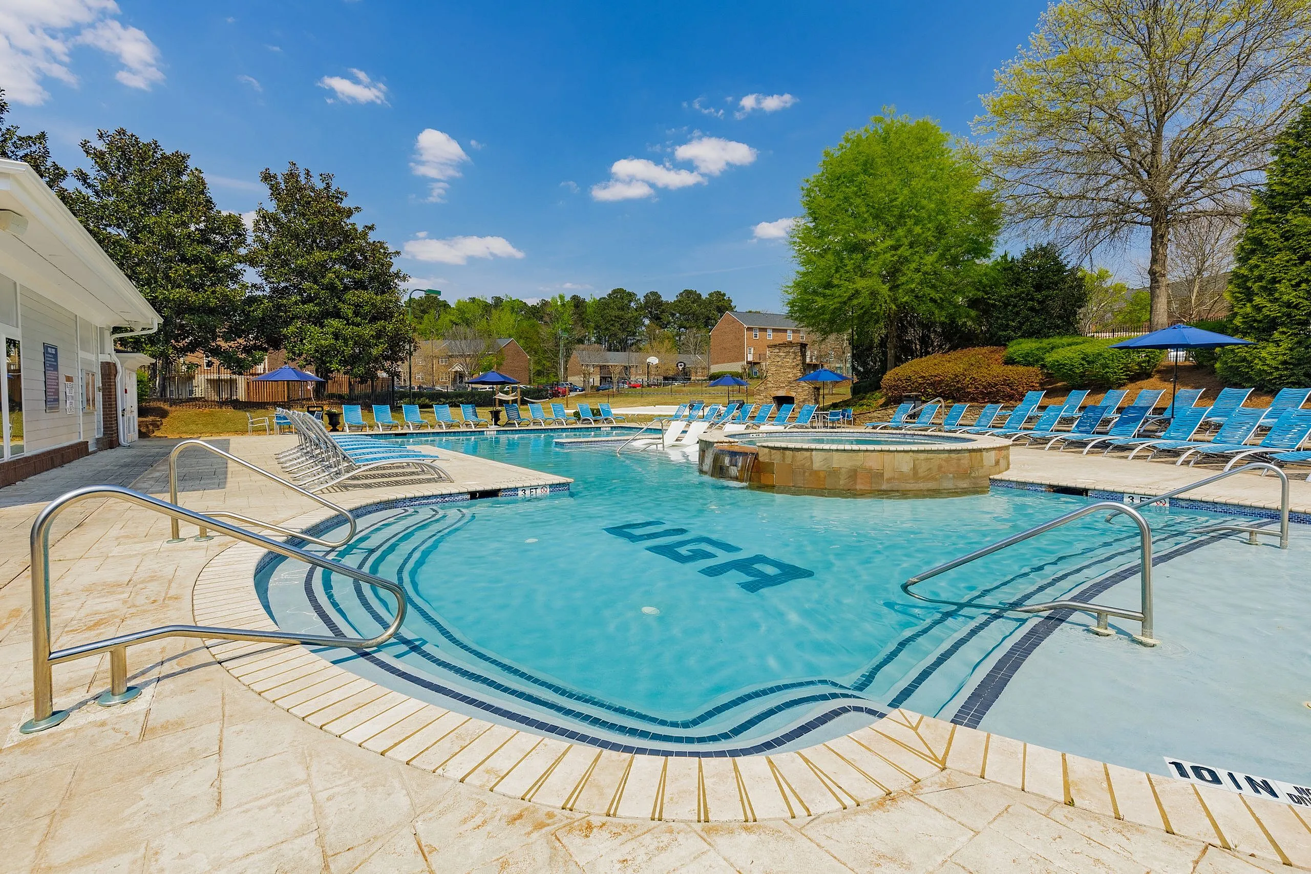 Luxurious outdoor pool area with pristine water, surrounded by vibrant greenery and ample lounging chairs under clear blue skies.