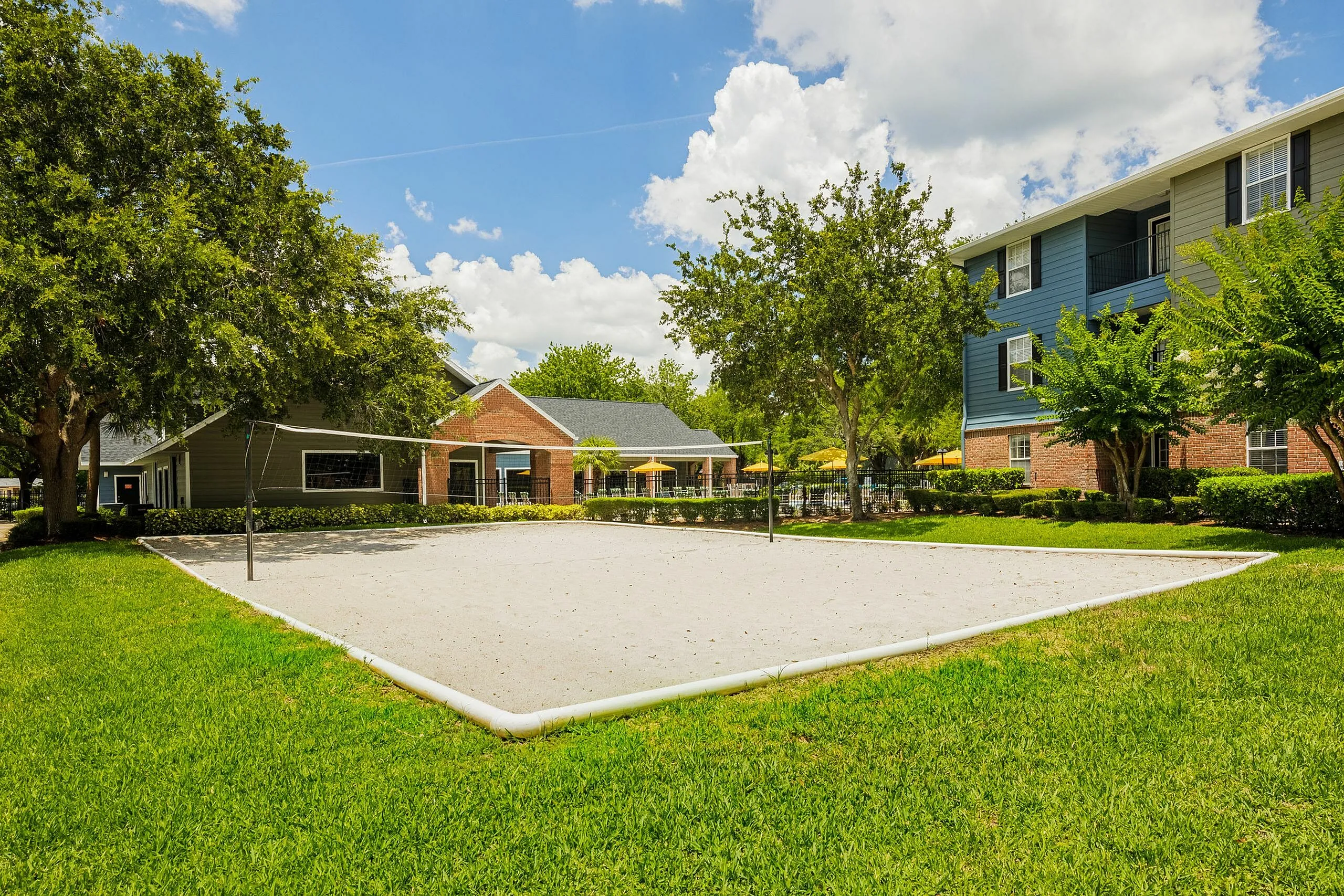 Inviting apartment complex featuring a lush green landscape, volleyball court, and charming residences under a bright blue sky.