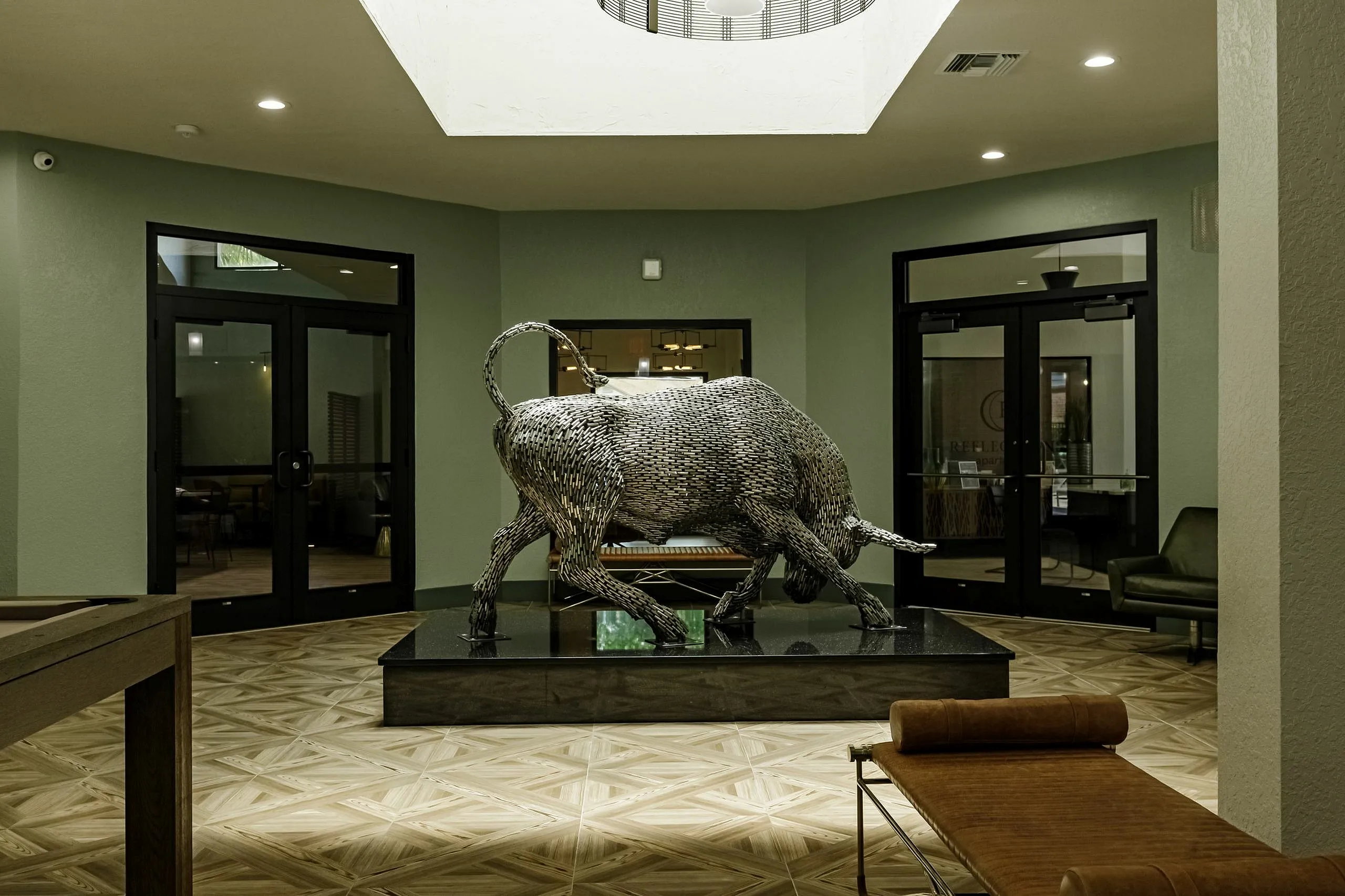 Elegant lobby with a striking metallic bull sculpture, modern design, and warm flooring, creating an inviting ambiance.