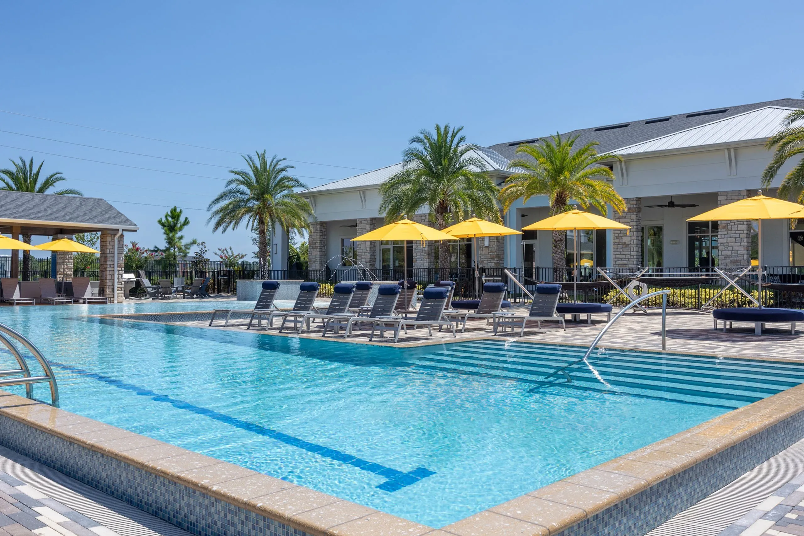 Luxurious apartment pool area with sparkling blue water, surrounded by stylish sun loungers and vibrant yellow umbrellas, set against a backdrop of palm trees and elegant architecture.